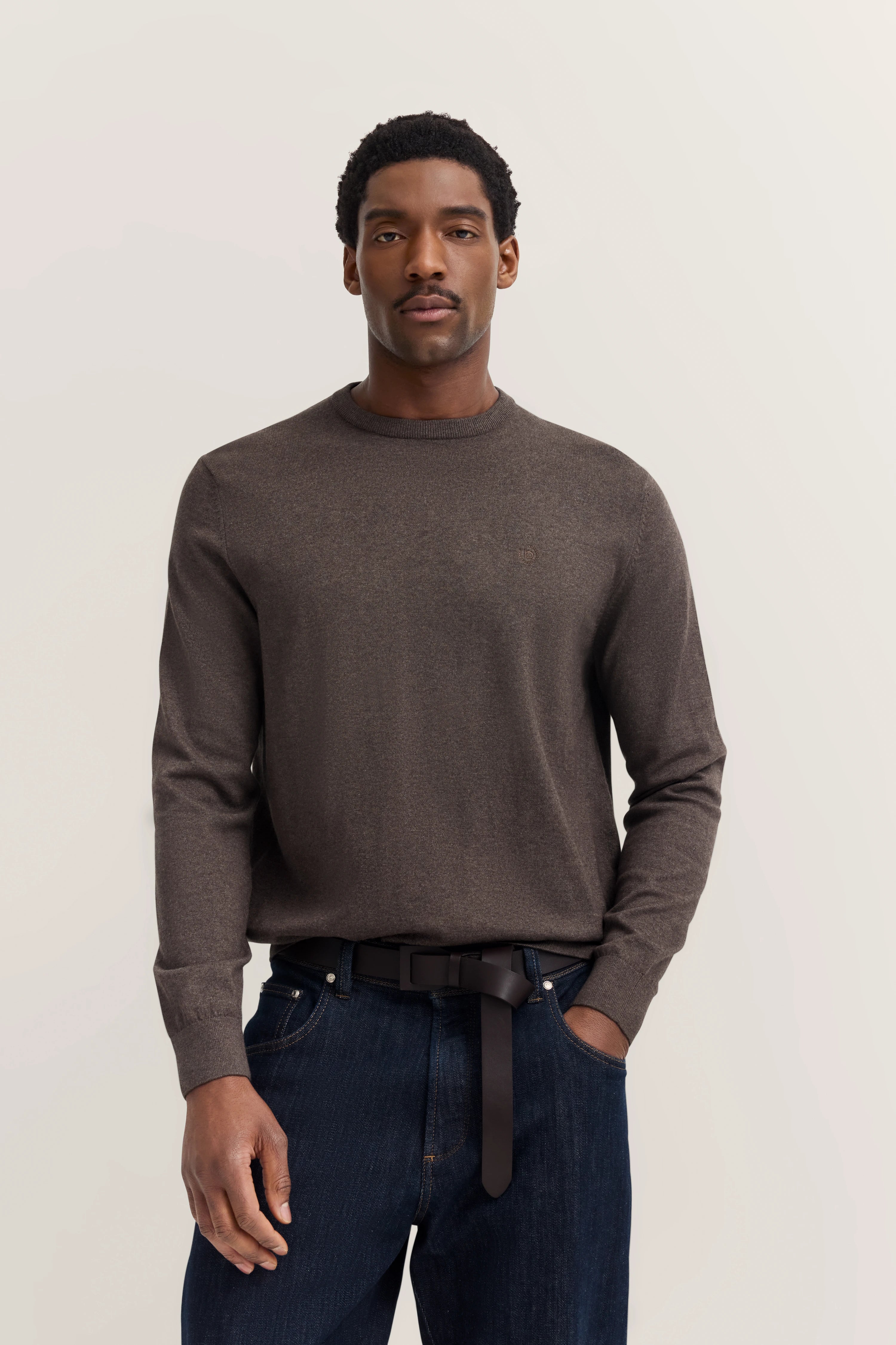 Modelafbeelding: Man in bruine bugatti trui, donkere jeans, ontspannen houding.