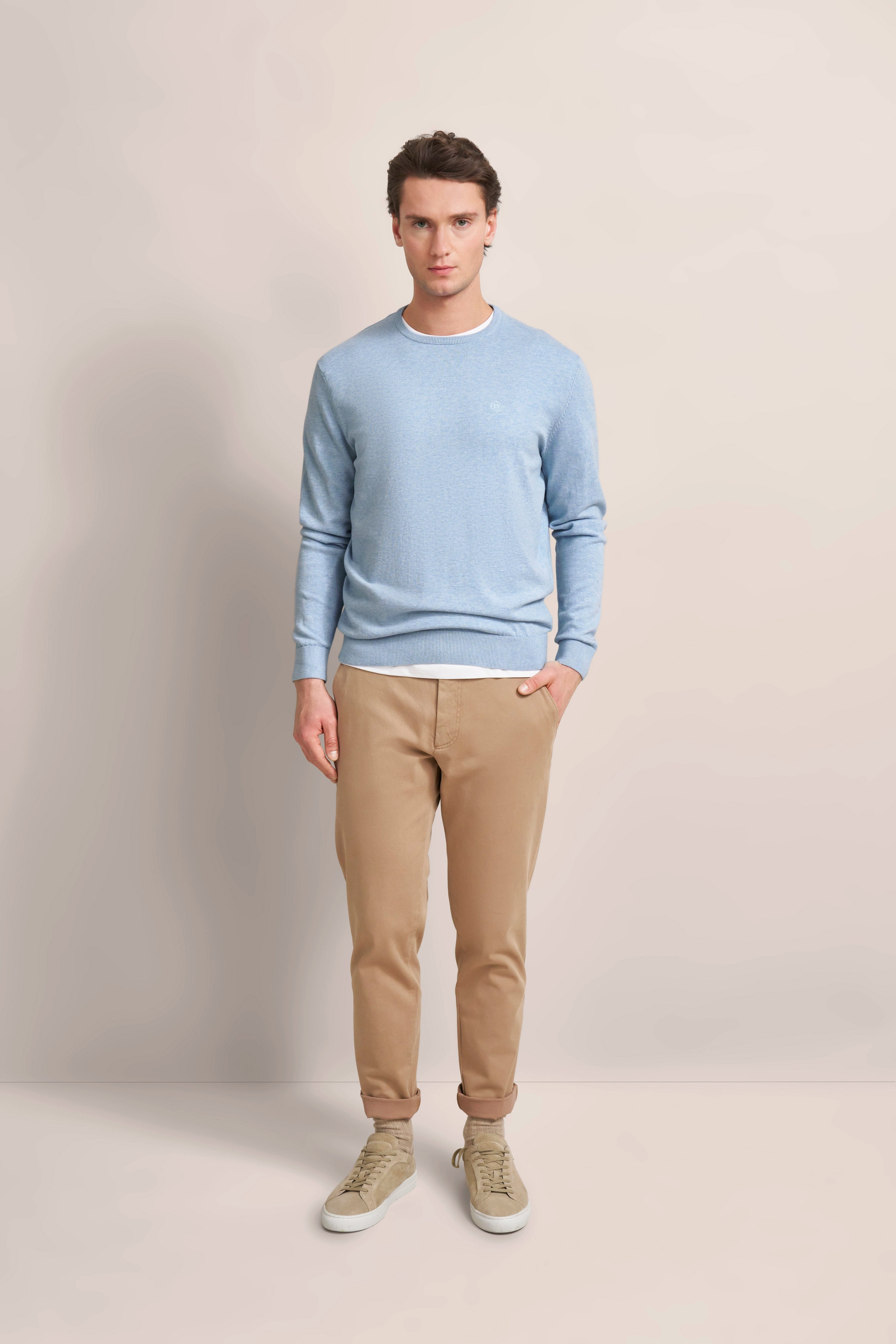 Model in hellblauem Pullover und beige Chinos, frontal stehend, casual Look.