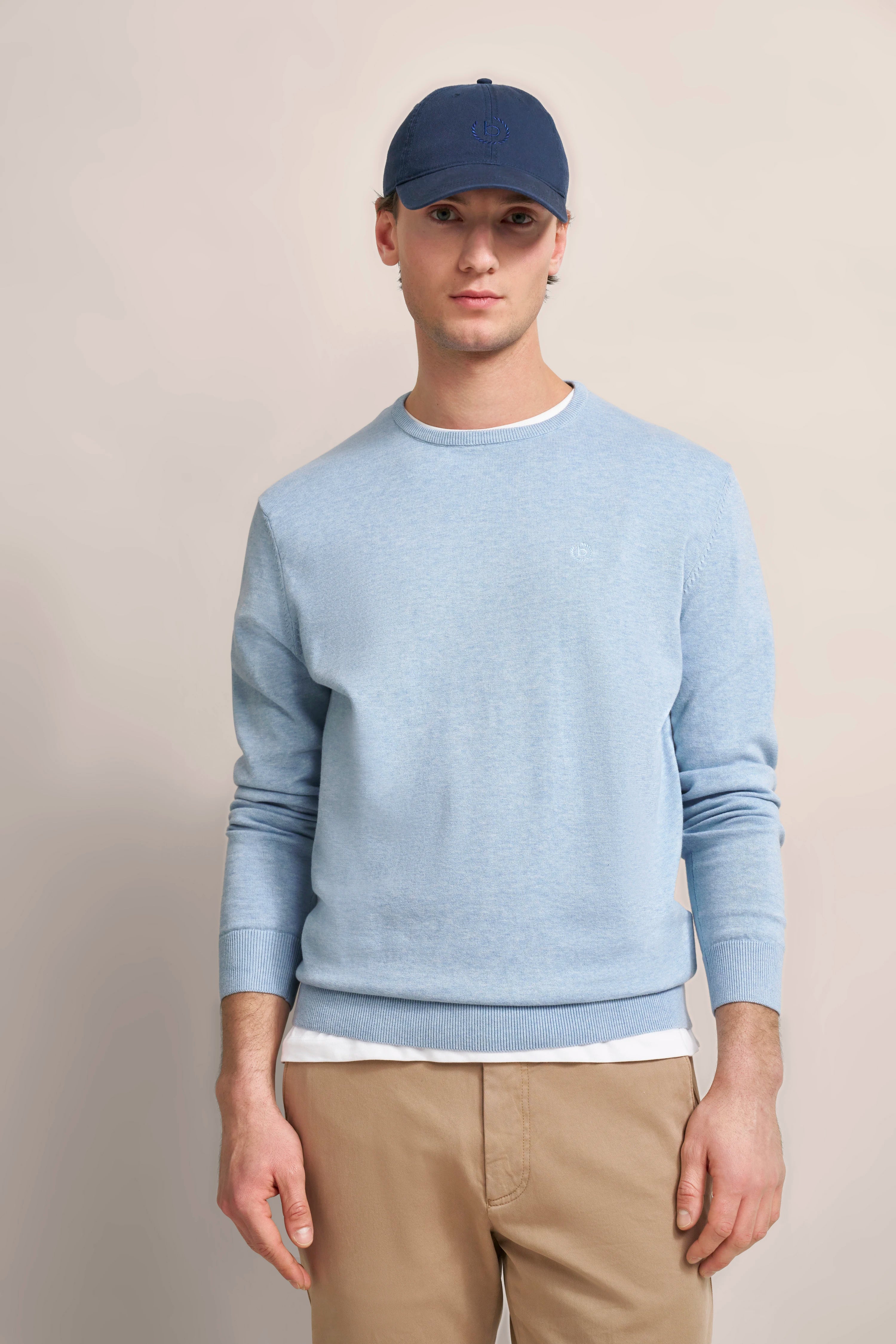 Blauer bugatti Pullover, beige Hose, dunkelblaue Cap, Modelbild, entspannte Pose.