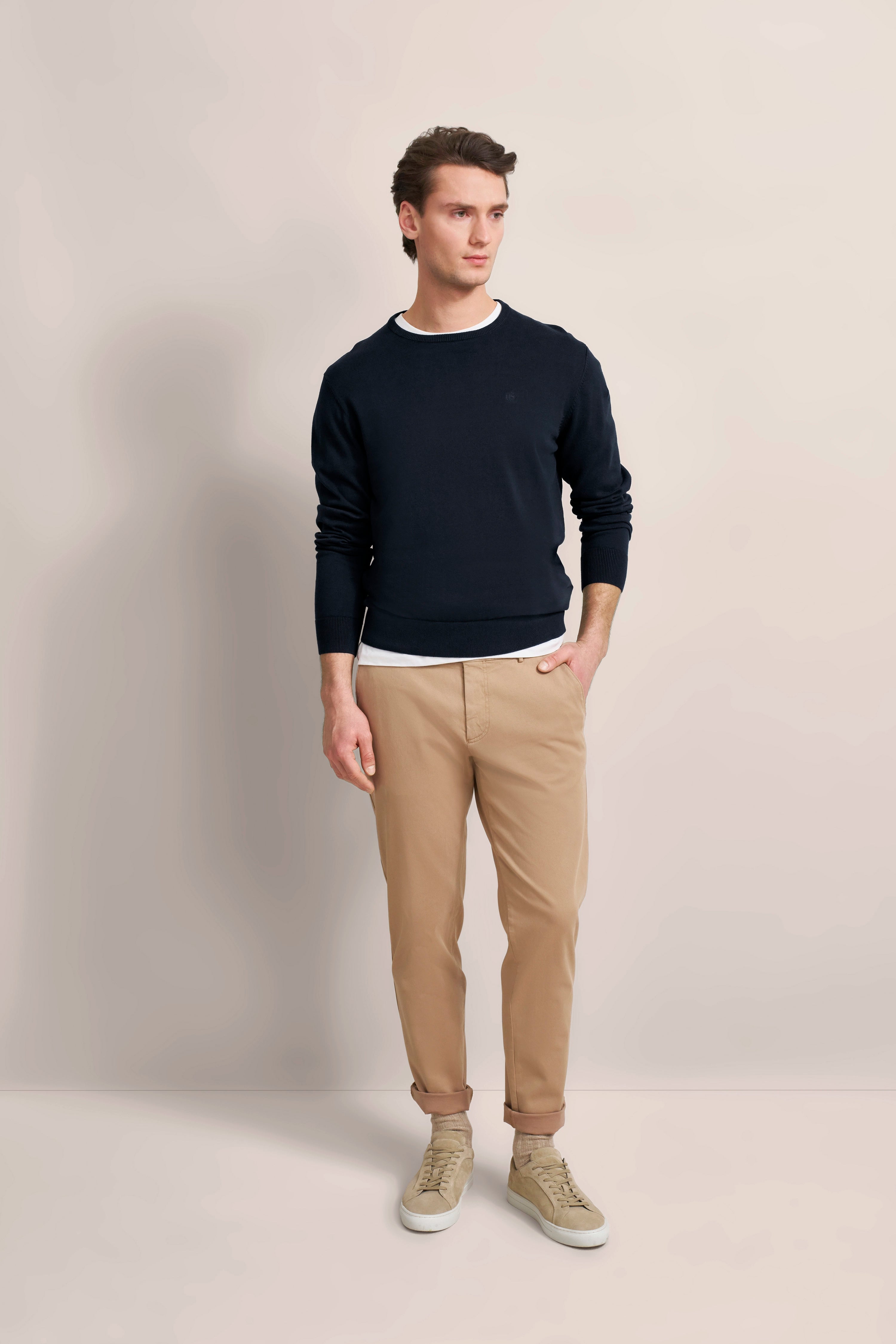 bugatti Modelbild: Dunkler Pullover, beige Chinos, lässige Pose, zeitlose Eleganz.