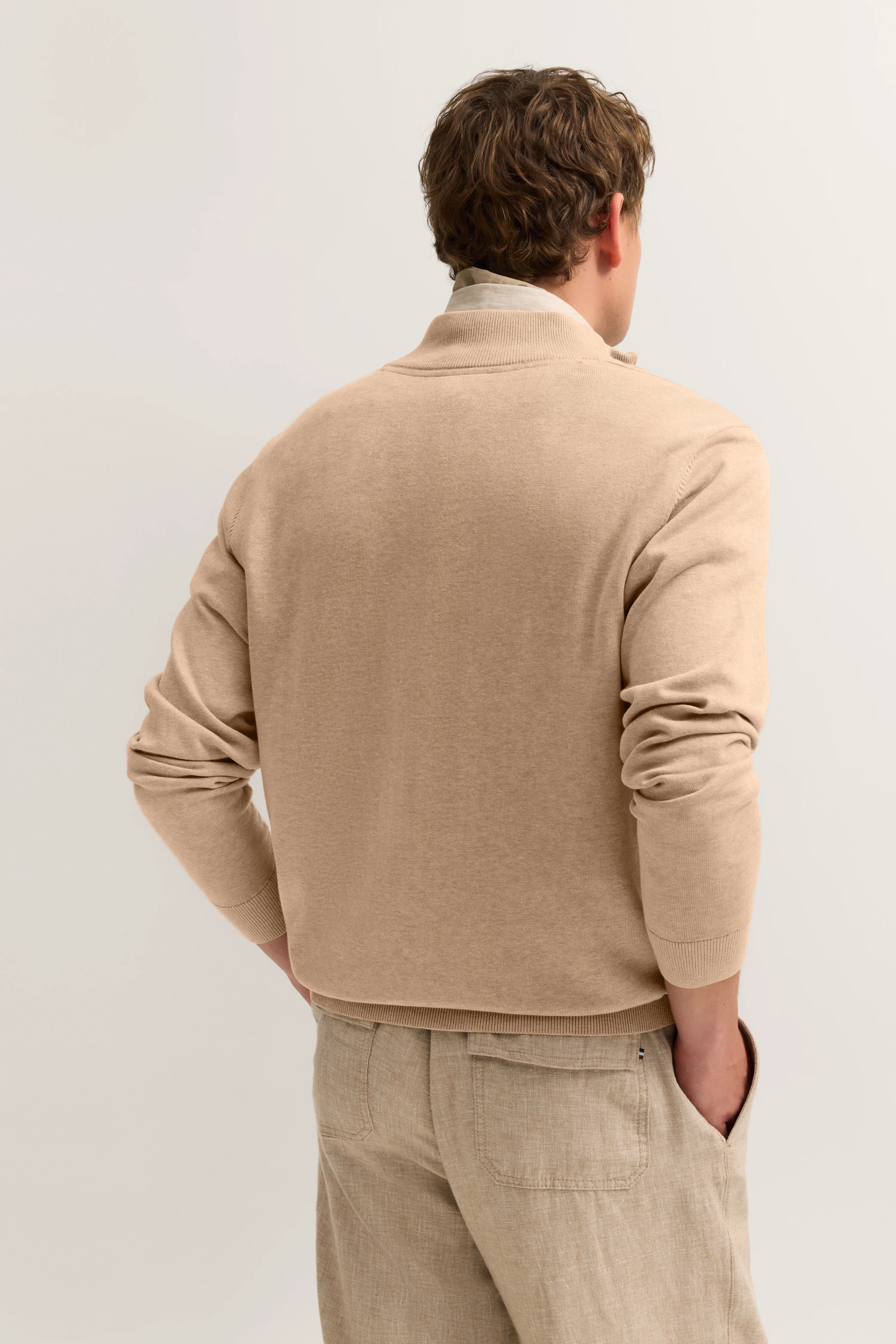 Beigefarbener bugatti Cardigan und Hose, Rückansicht, Modell leger mit Händen in den Taschen.