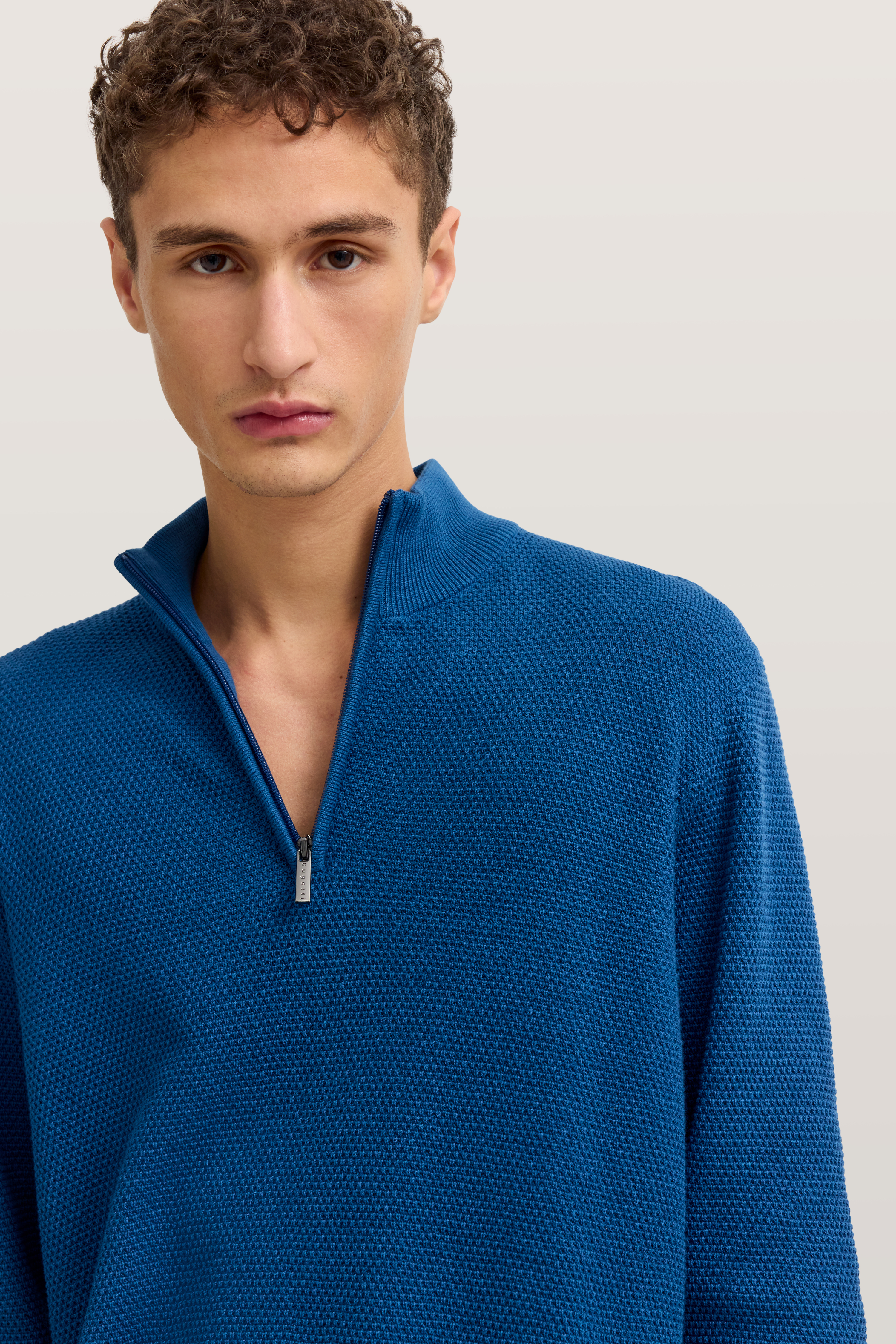 Blaues bugatti Strickoberteil mit Reißverschluss, Modelbild, neutraler Gesichtsausdruck.