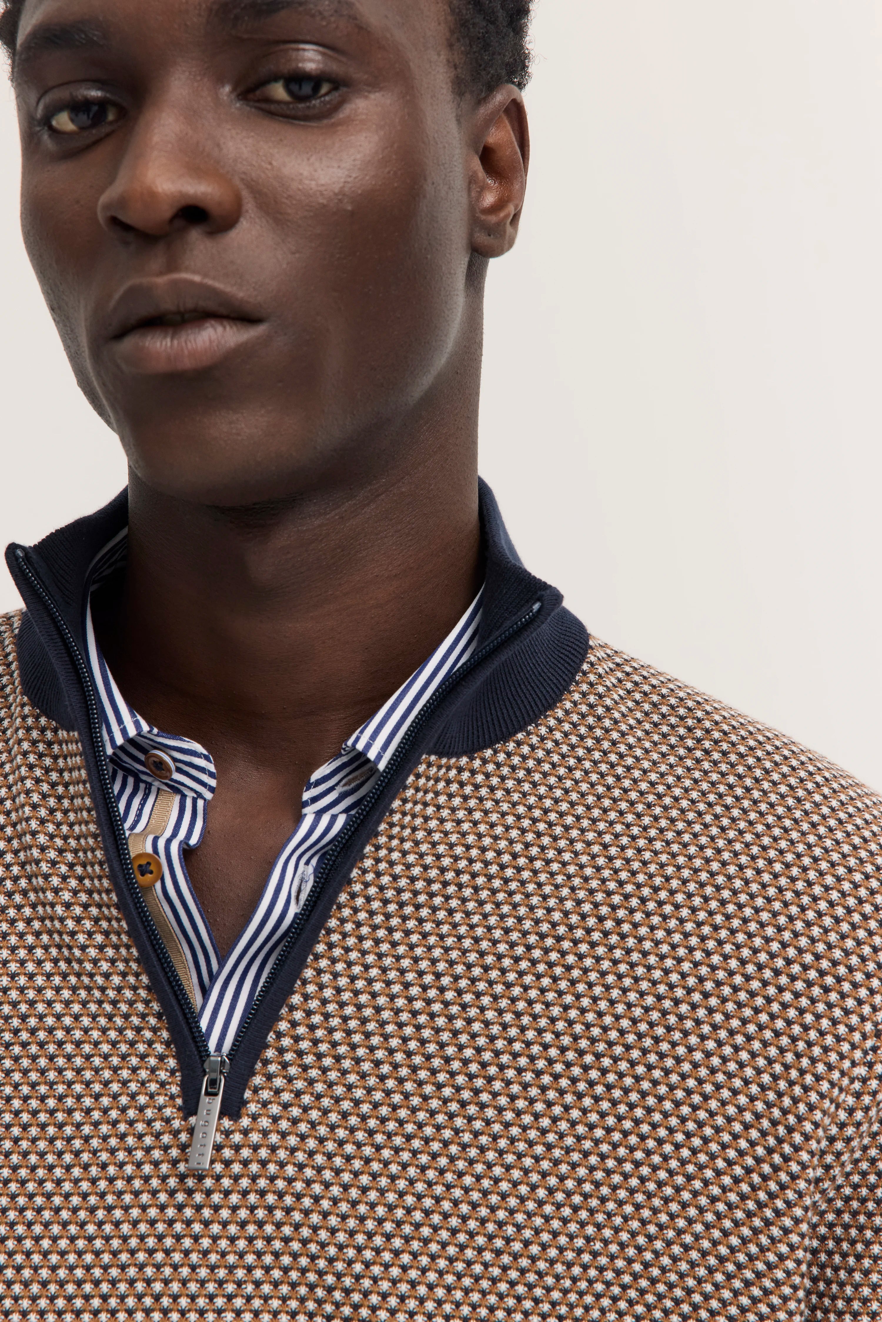 Büstenbild: Model trägt bugatti Strickpullover mit geometrischem Muster, gestreiftes Hemd darunter.