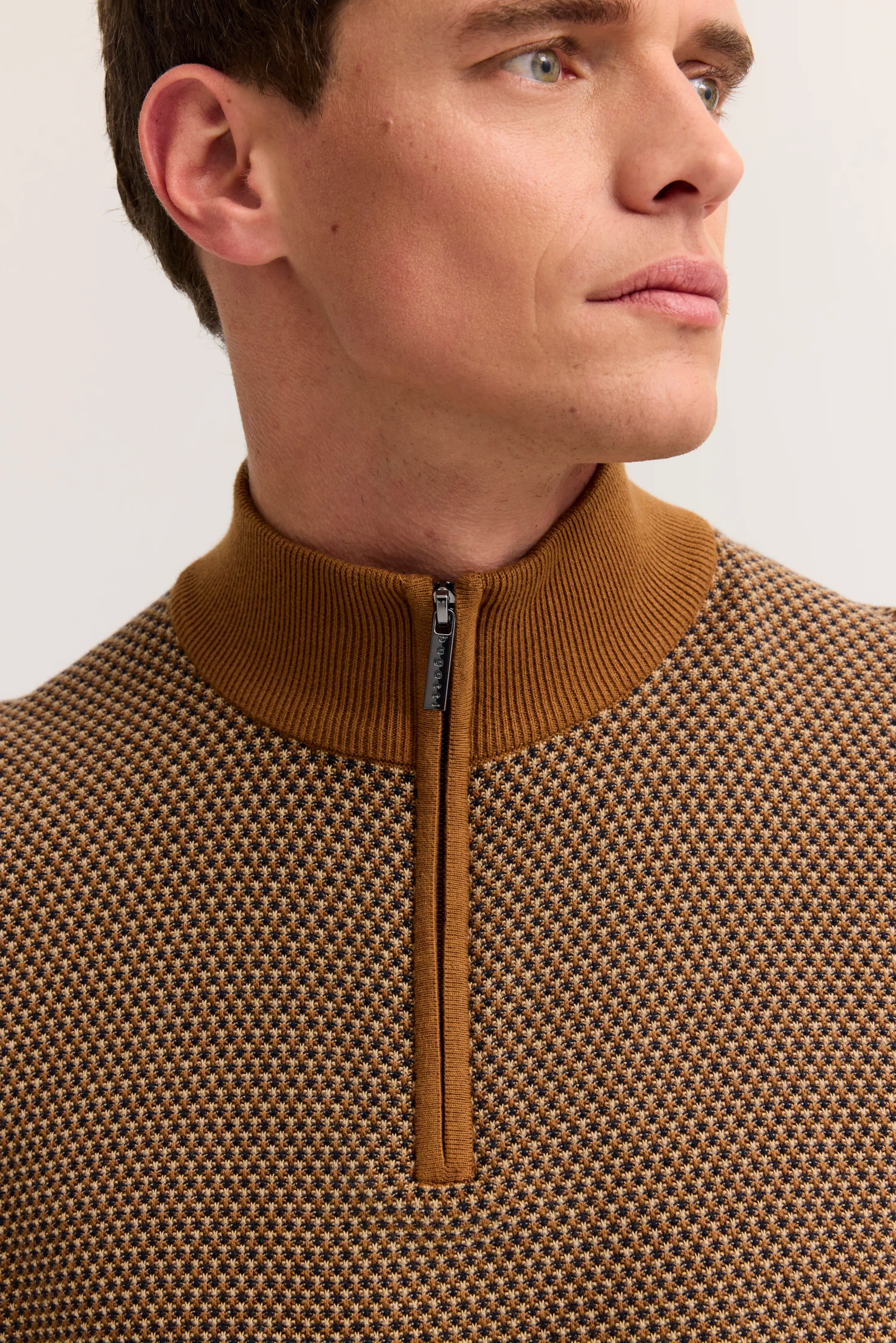 Herrenmodel von hinten in braunem Musterpullover und beigen Chinos.