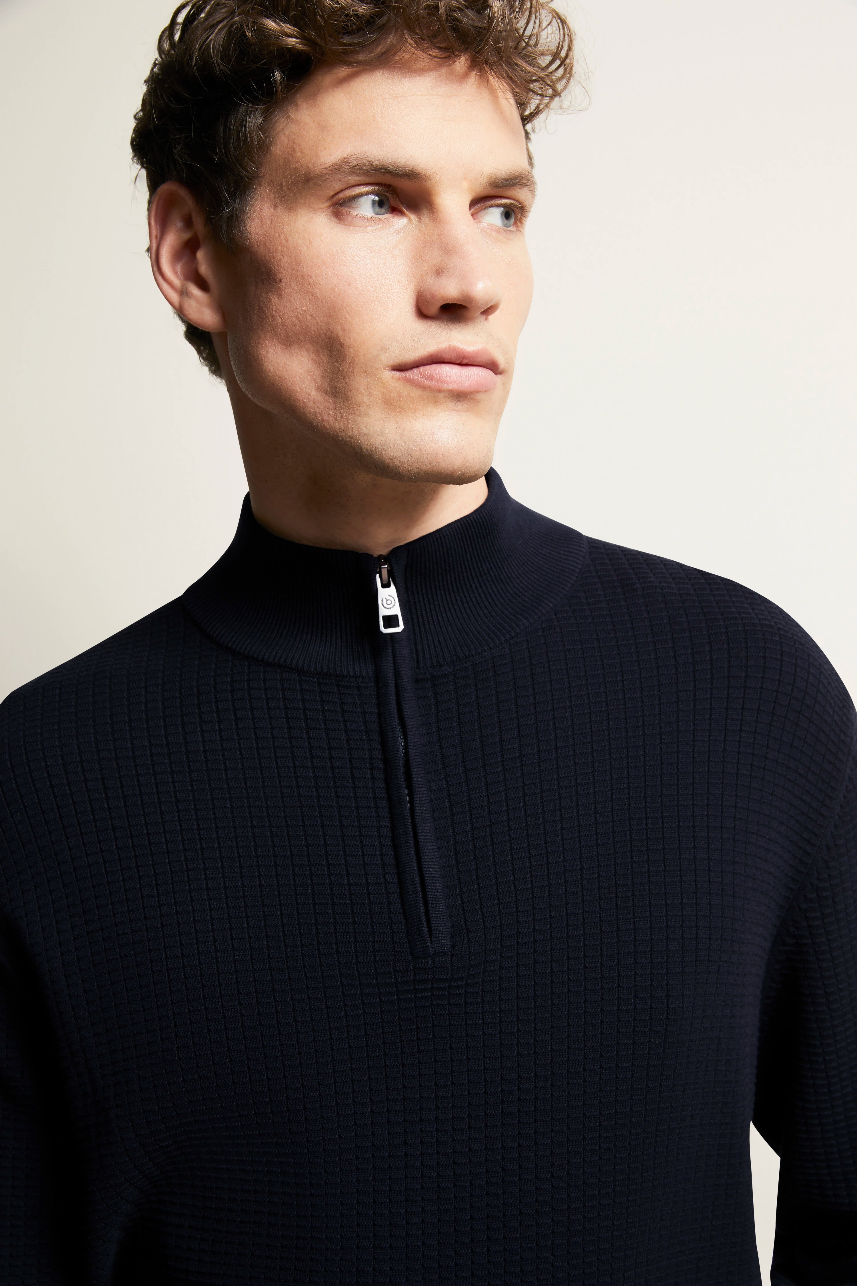 Model in dunkelblauem bugatti Pullover mit Stehkragen und Reißverschluss vor neutralem Hintergrund.