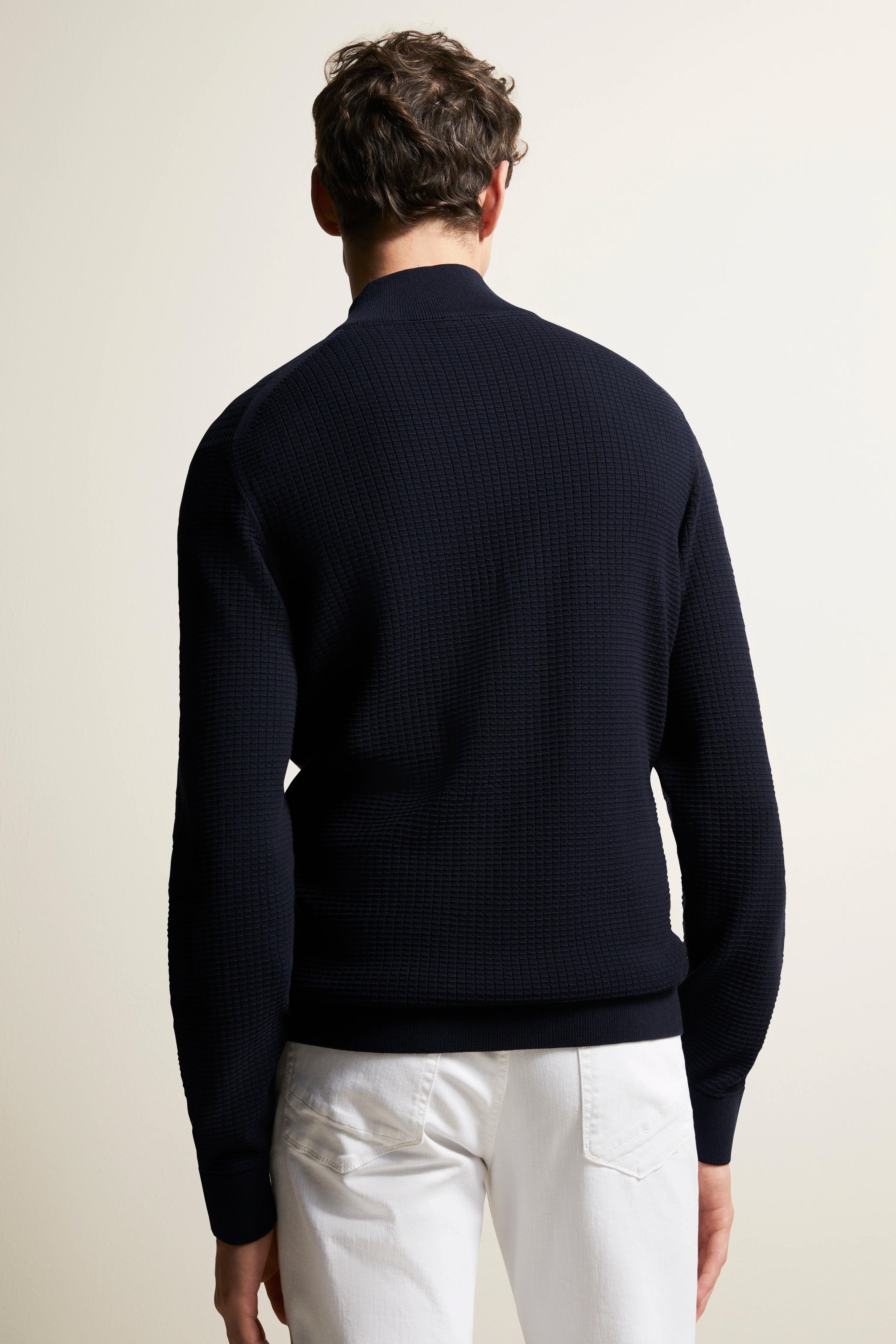 Navy Pullover mit Strukturmuster, weißer Hose, Modelbild von hinten, entspanntes Posing.