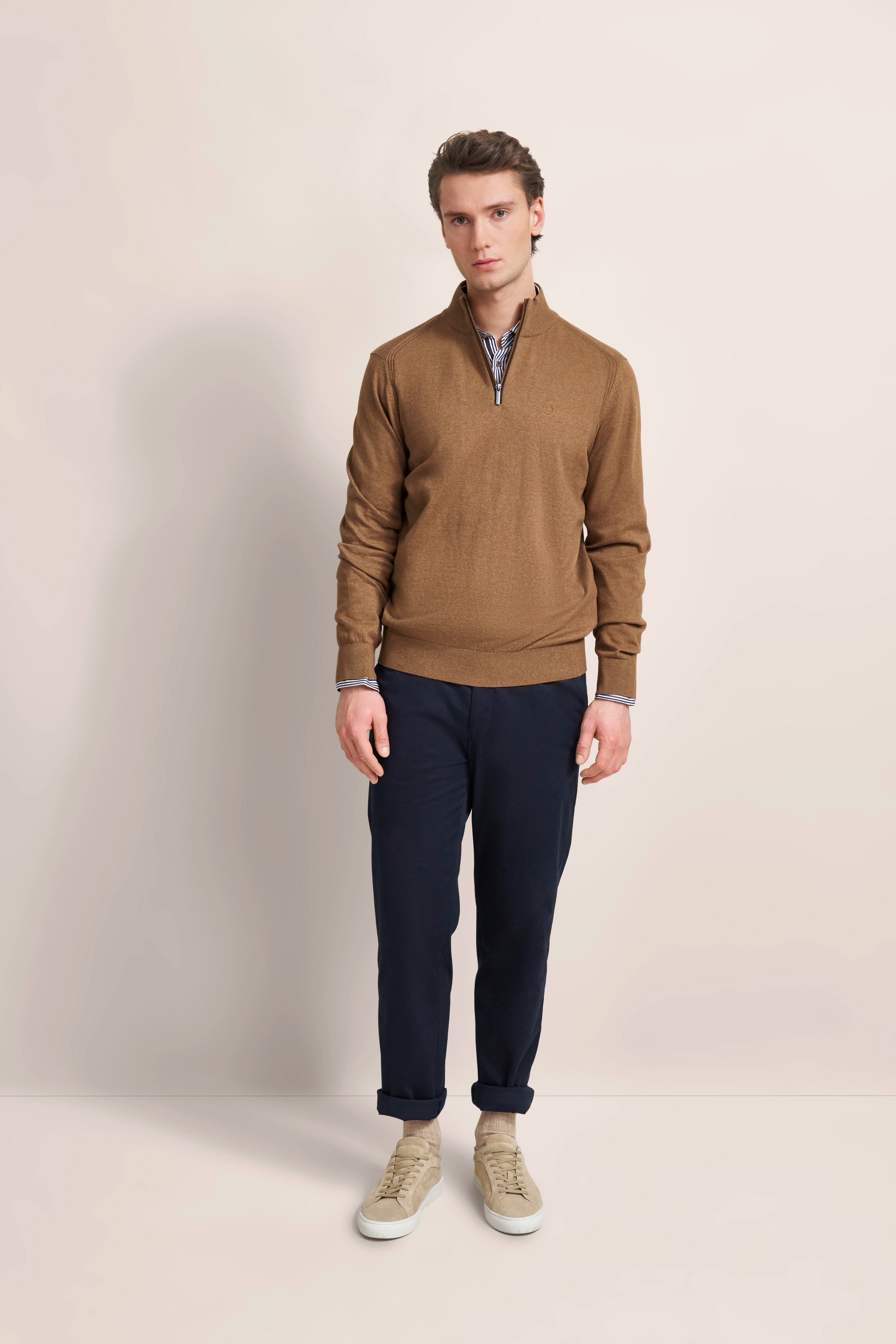 Brauner bugatti Pullover, dunkelblaue Hose, beige Sneakers. Modelbild, entspanntes Posing.