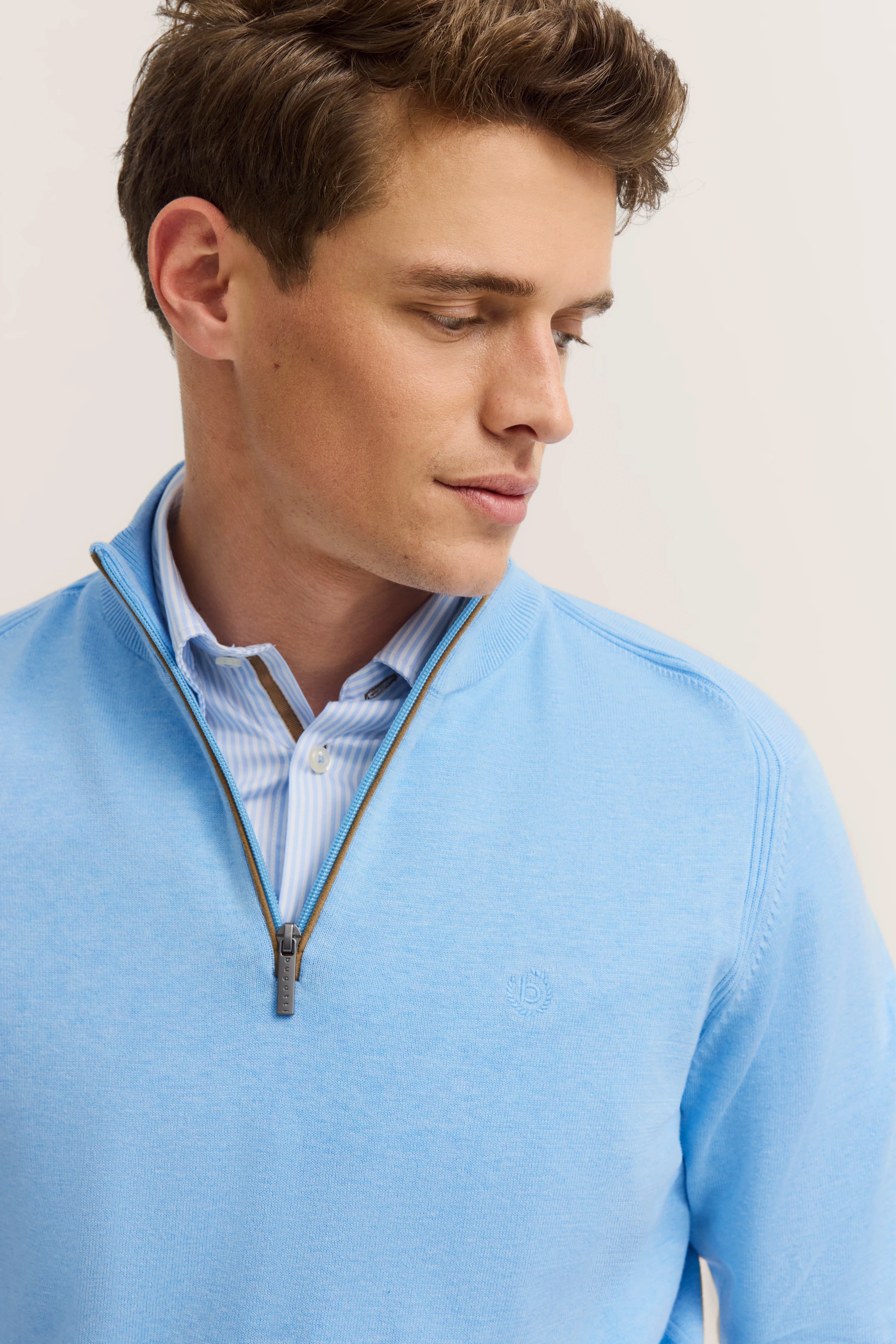 Blauwe bugatti trui met rits over gestreept overhemd, modelpose, ontspannen uitstraling.