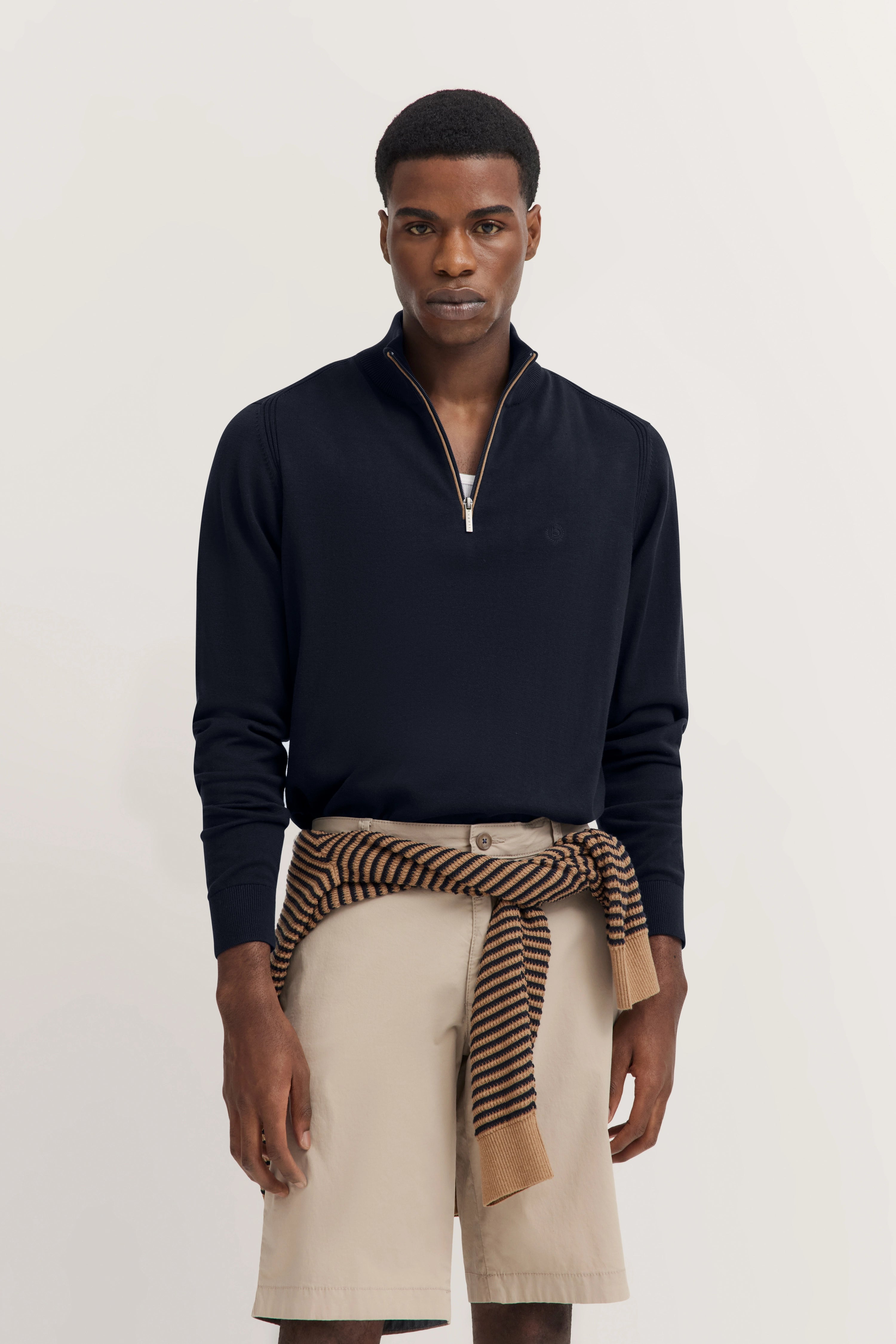 Model met navy langarmshirt, beige shorts, gestreepte trui om de taille. Ontspannen, stijlvol.