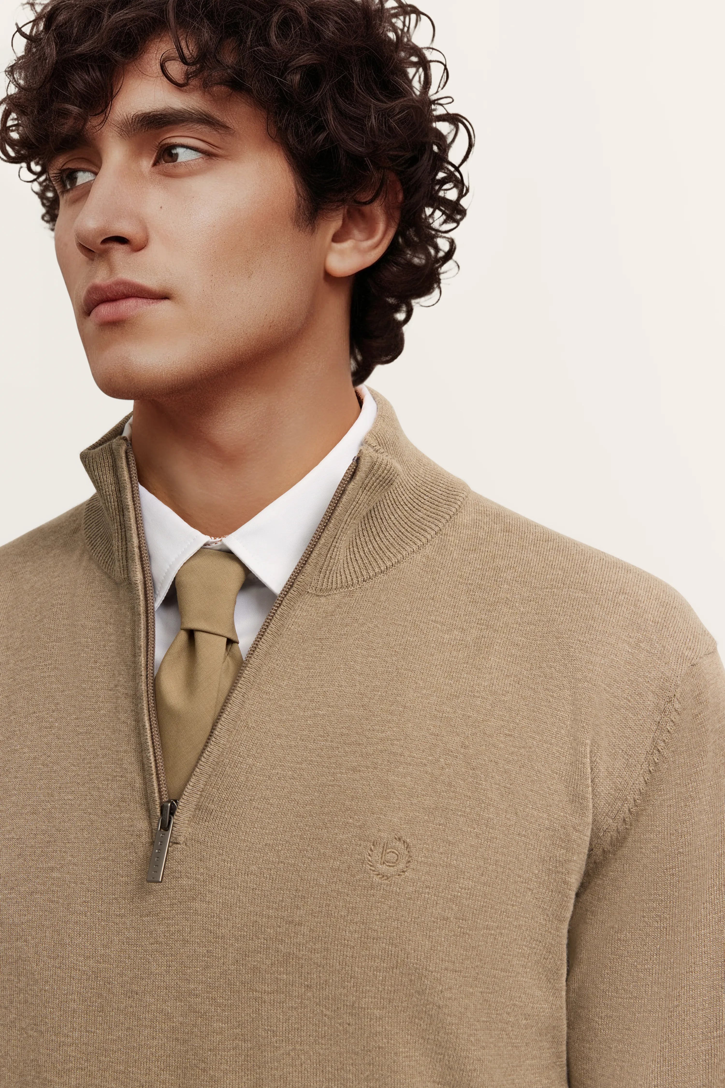 Beigefarbener bugatti Pullover mit Reißverschluss, weißem Hemd und passender Krawatte, Modelbild im Halbprofil.