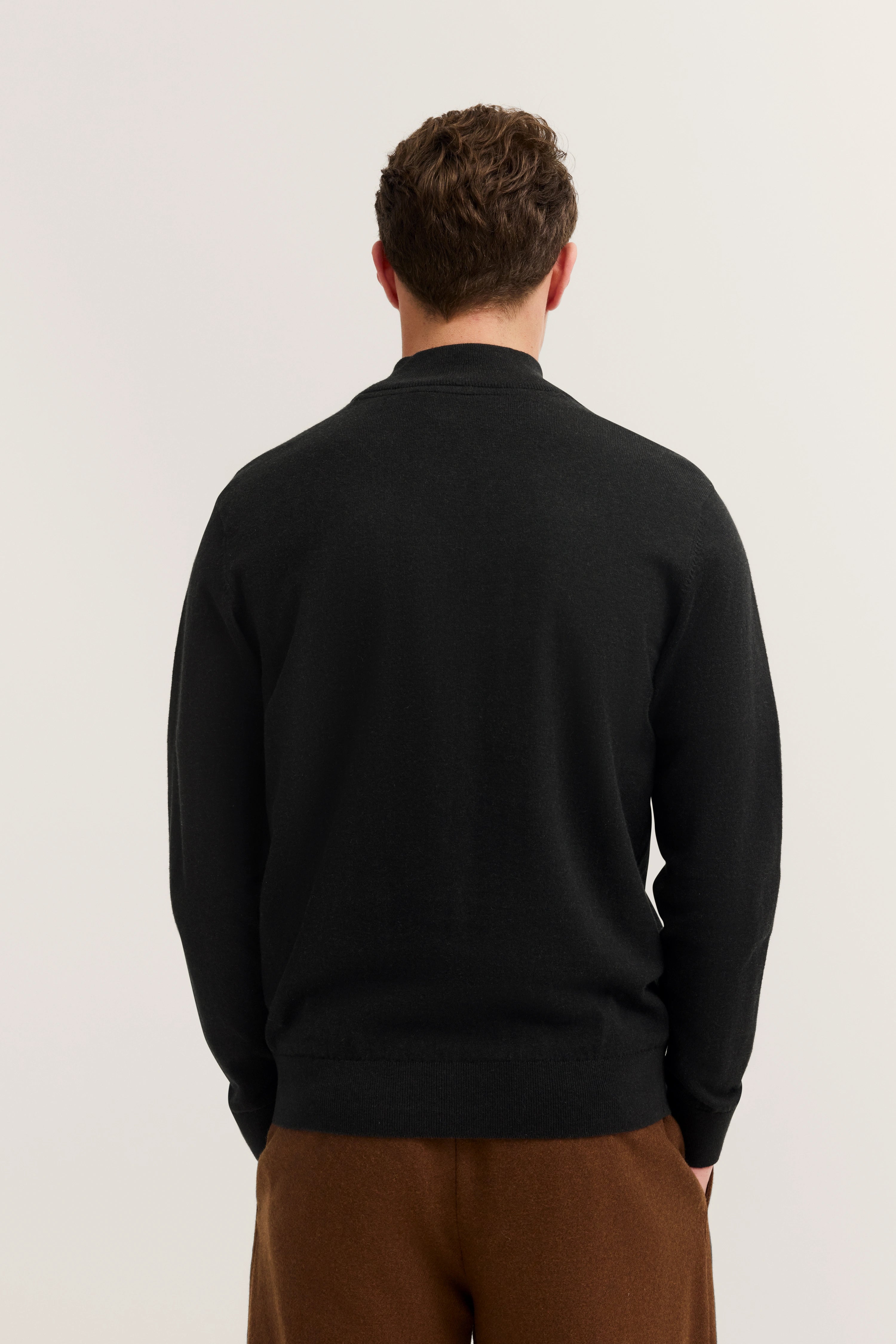 Schwarzer bugatti Pullover, Rückansicht, kombiniert mit brauner Hose. Modelbild, entspannt stehend.