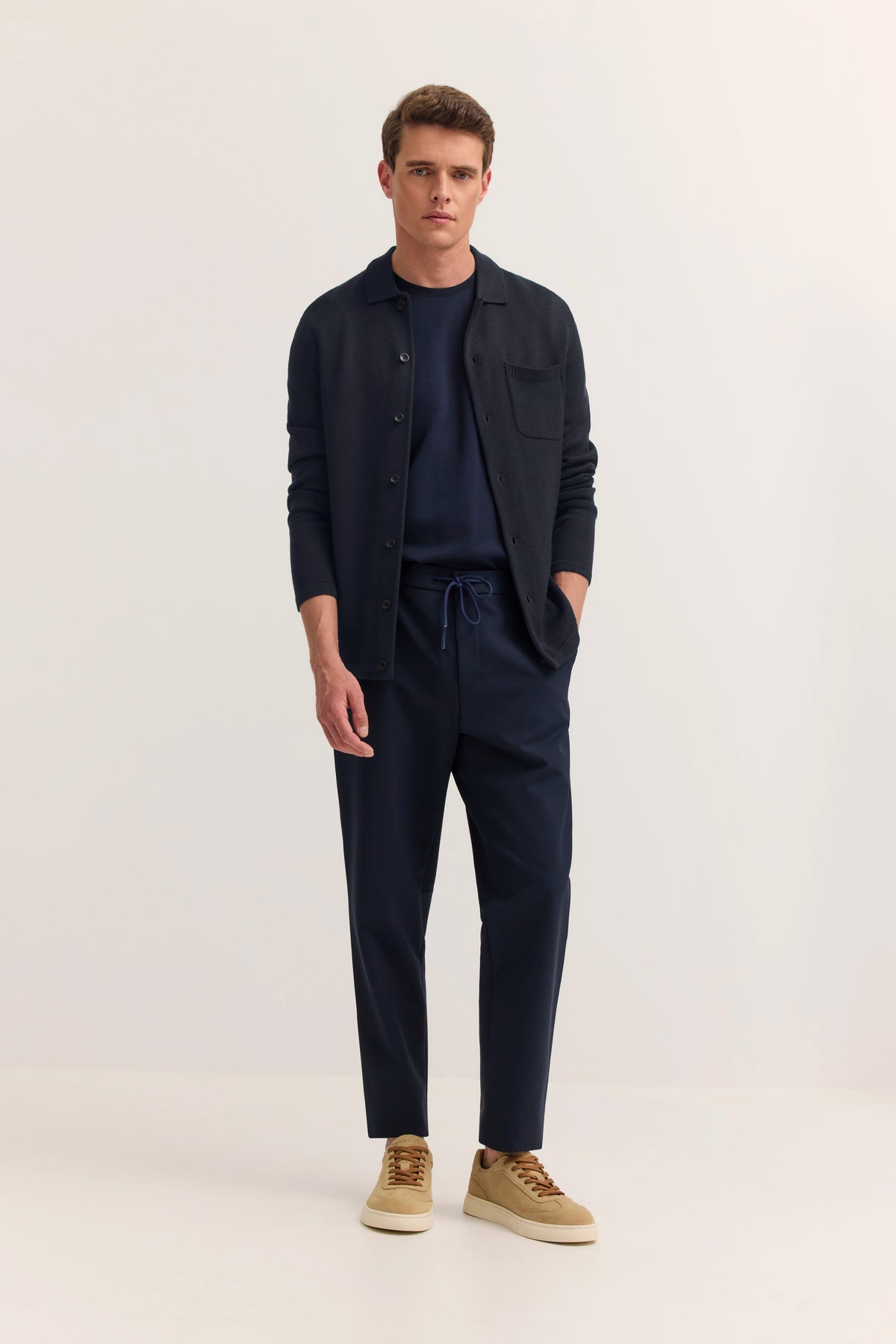 Navy bugatti Outfit: Hemd, Hose. Model in entspannter Pose, Hände in Taschen, beige Sneaker.