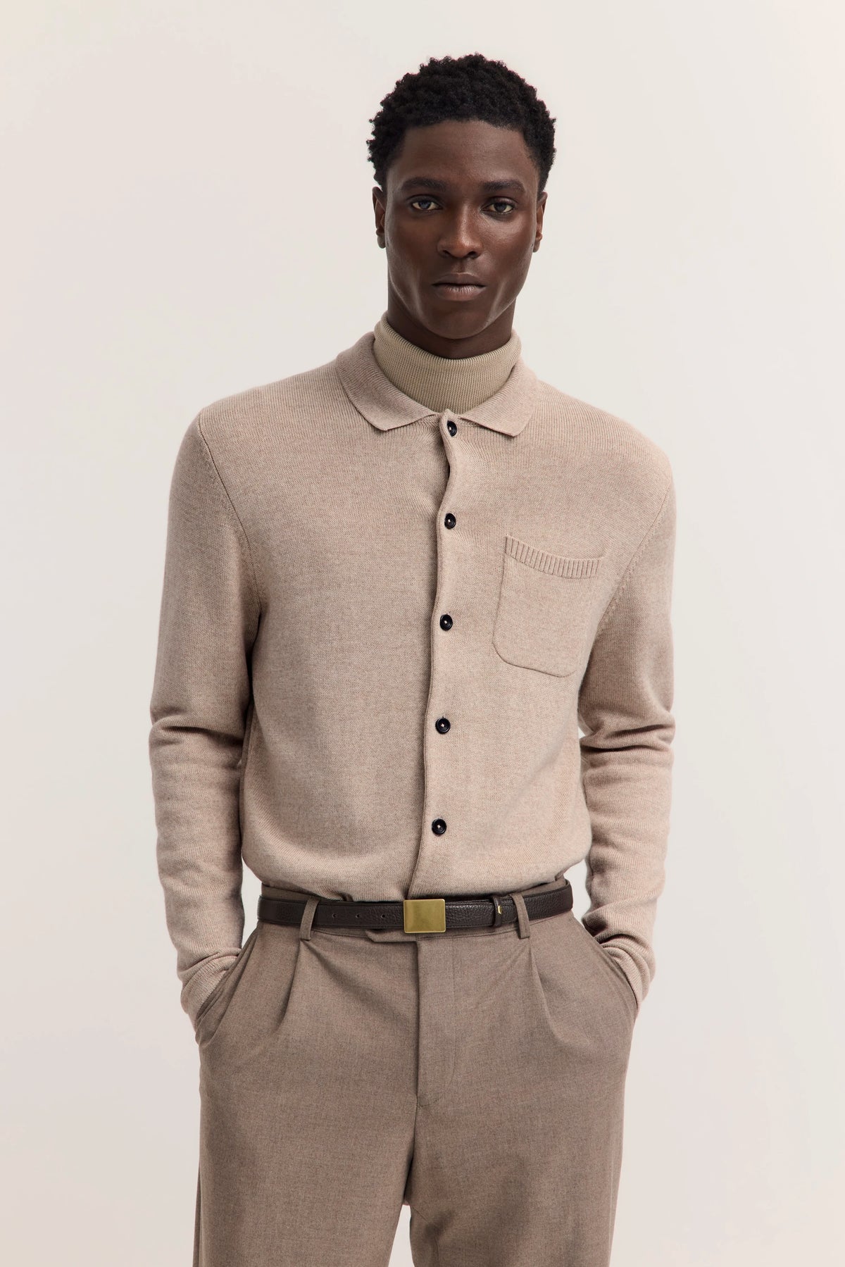 Elegantes Model-Outfit in Beige mit Strickjacke und Rollkragenpullover, entspannte Pose.