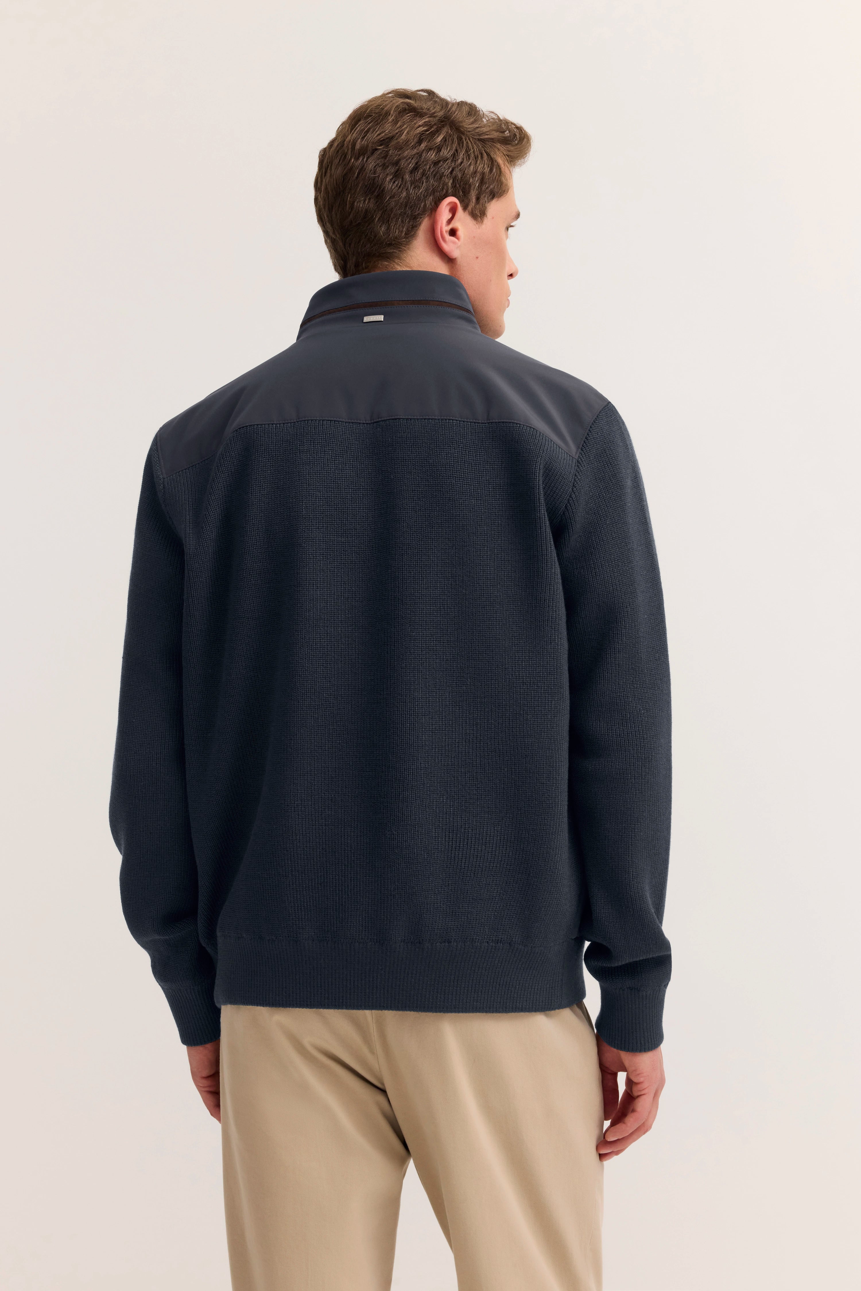 bugatti Herrenoutfit, dunkelblauer Pullover, beige Hose, Modelbild von hinten.