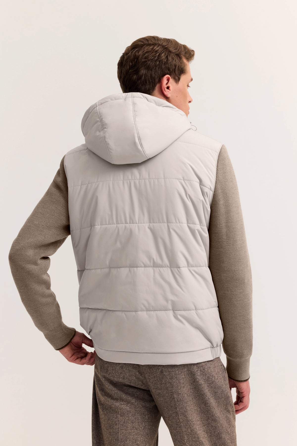 bugatti Model in grauer Weste und beige Strickpullover, Rückansicht, entspannte Pose.