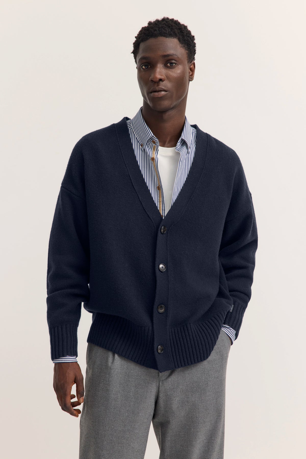 Model in grauem Cardigan, gestreiftem Hemd und grauer Hose von bugatti, legeres Posing.