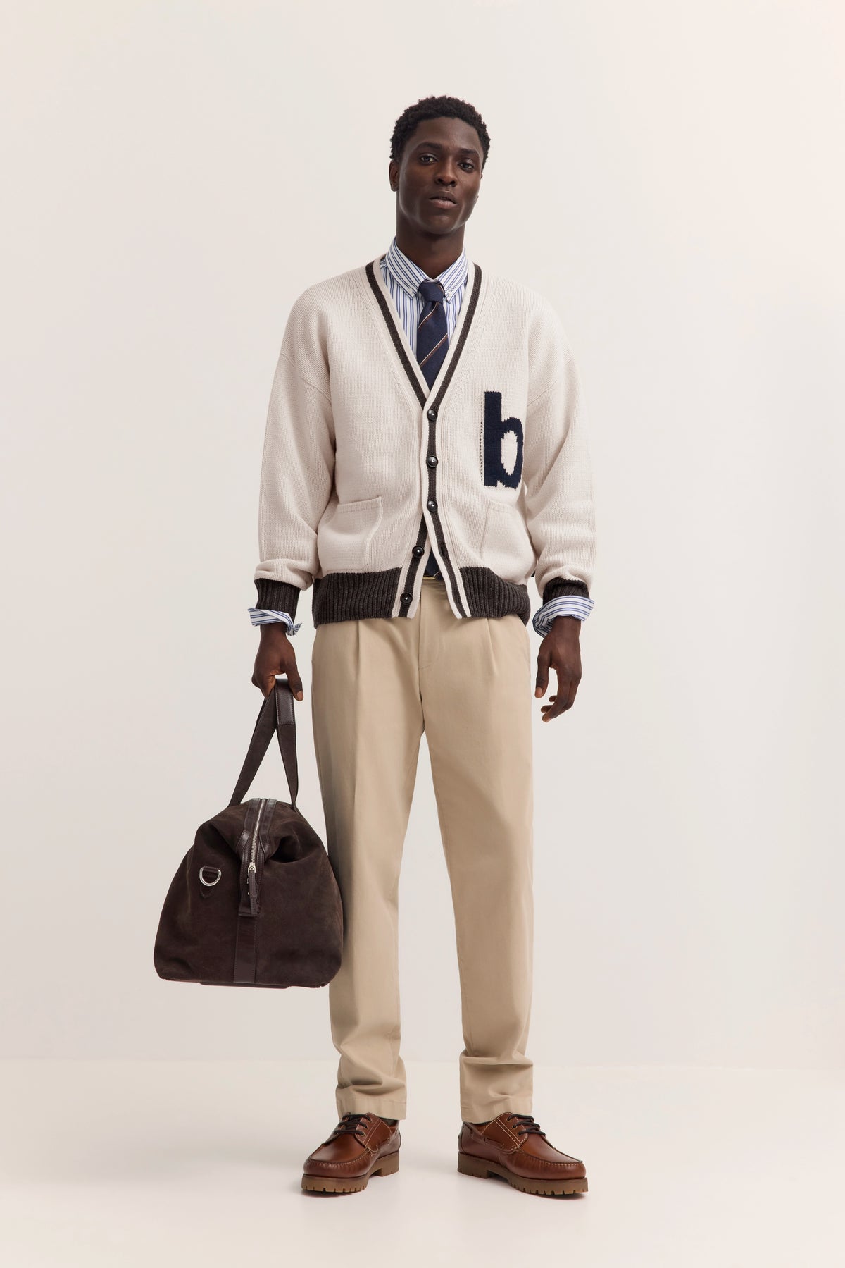 Model in beige bugatti Cardigan, gestreiftem Hemd und Krawatte, beige Hose, braune Schuhe, lässig stehend.