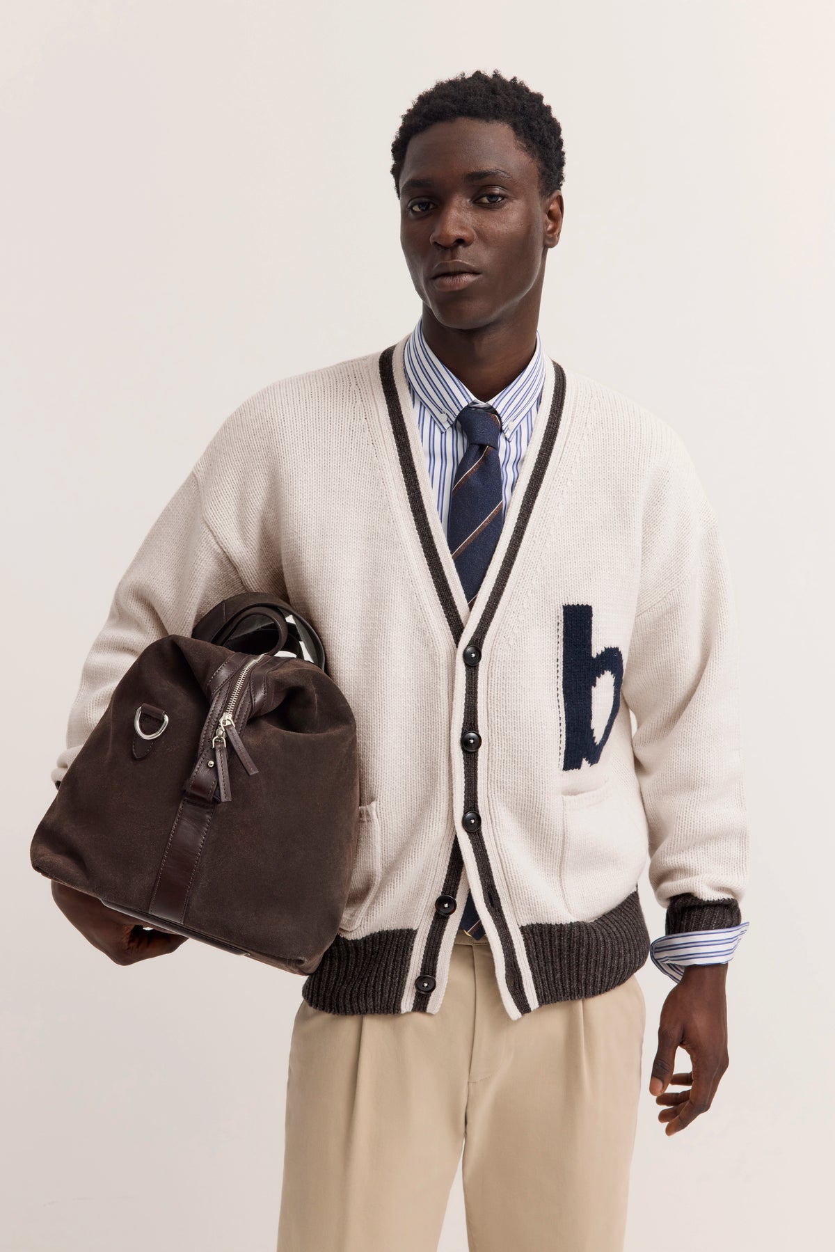 Modelbild mit bugatti Cardigan in Weiß, gestreiftem Hemd, Krawatte und beigefarbener Hose. Model hält braune Tasche.