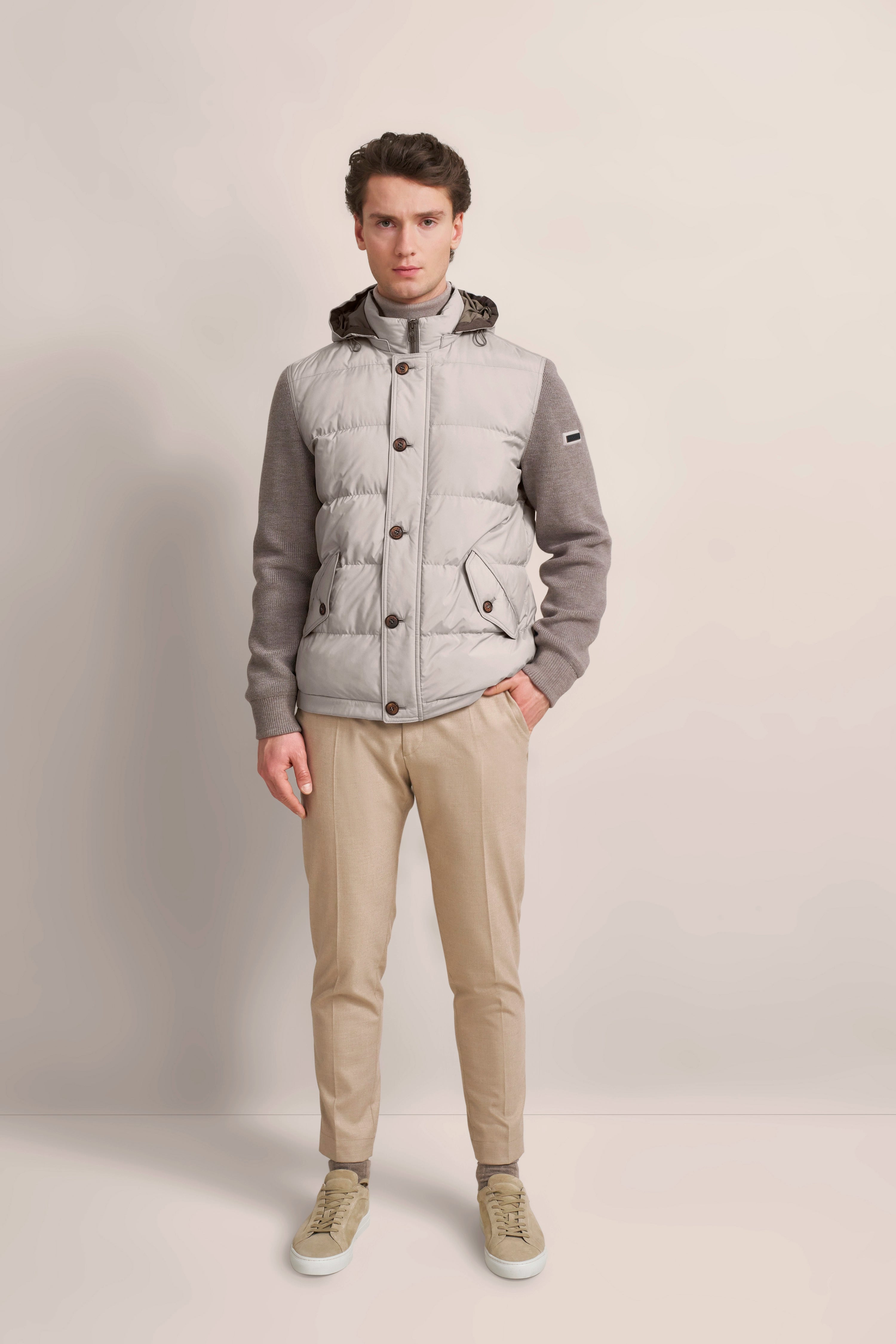 Model in grauer bugatti-Jacke, beige Hose und Sneakers. Stehende Pose, modern und stilvoll.
