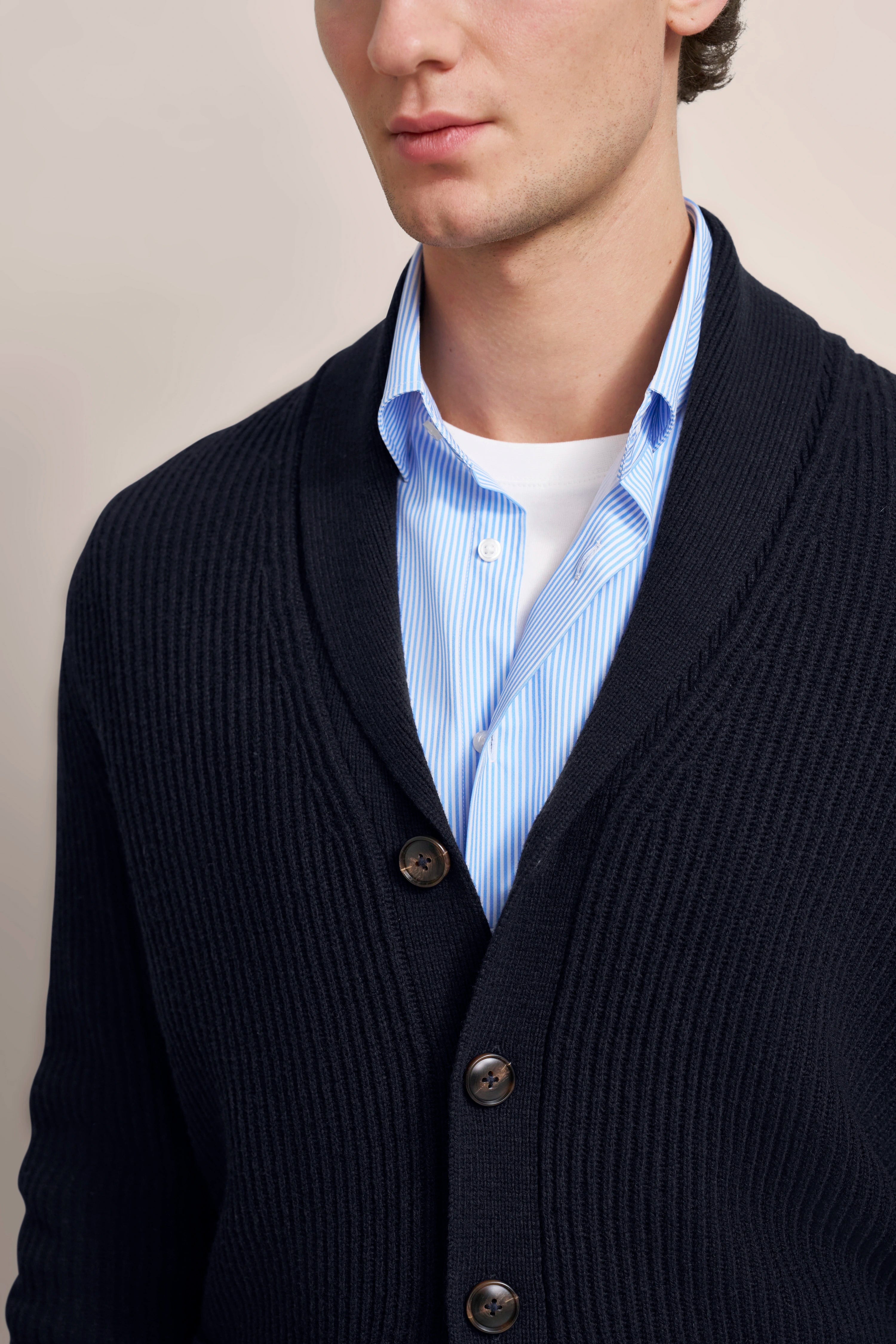 bugatti Modell in dunkelblauer Strickjacke, blau-weiß gestreiftes Hemd, entspanntes Posing.