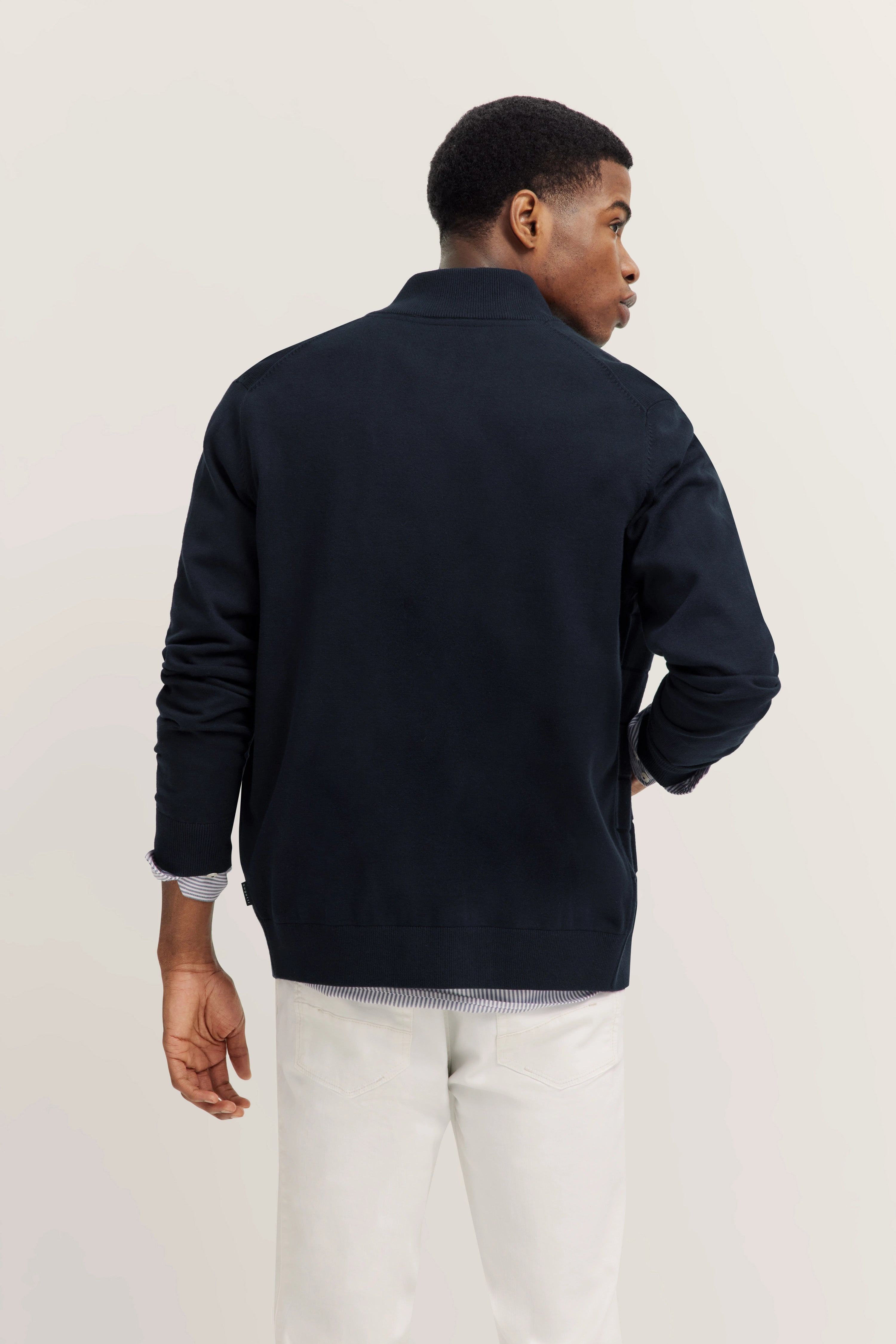 Model draagt een zwarte jas en witte broek van bugatti, achteraanzicht, casual pose.