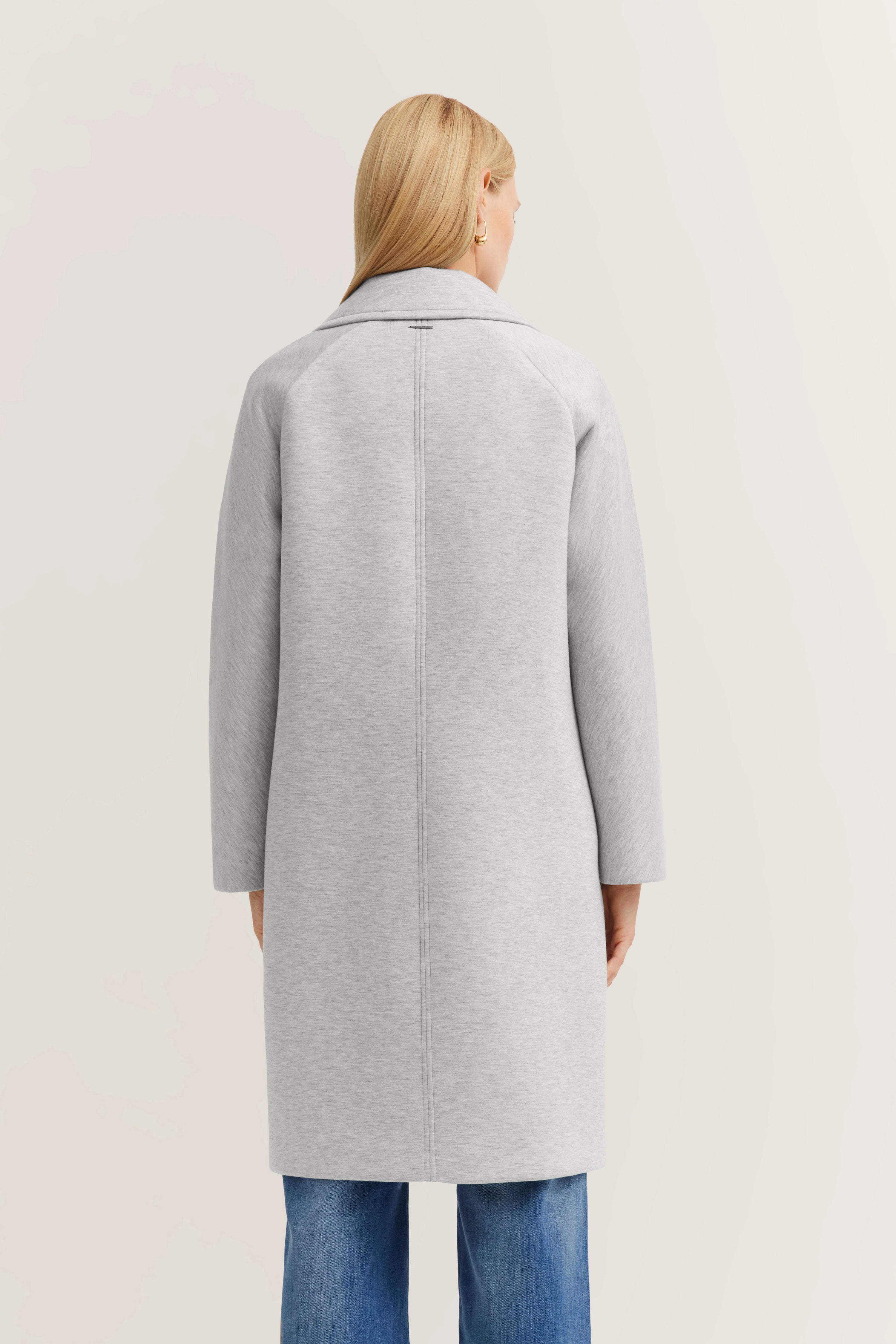 Grauer bugatti Mantel, Rückansicht auf Model. Mantel über blauer Jeans, lässig und stilvoll.
