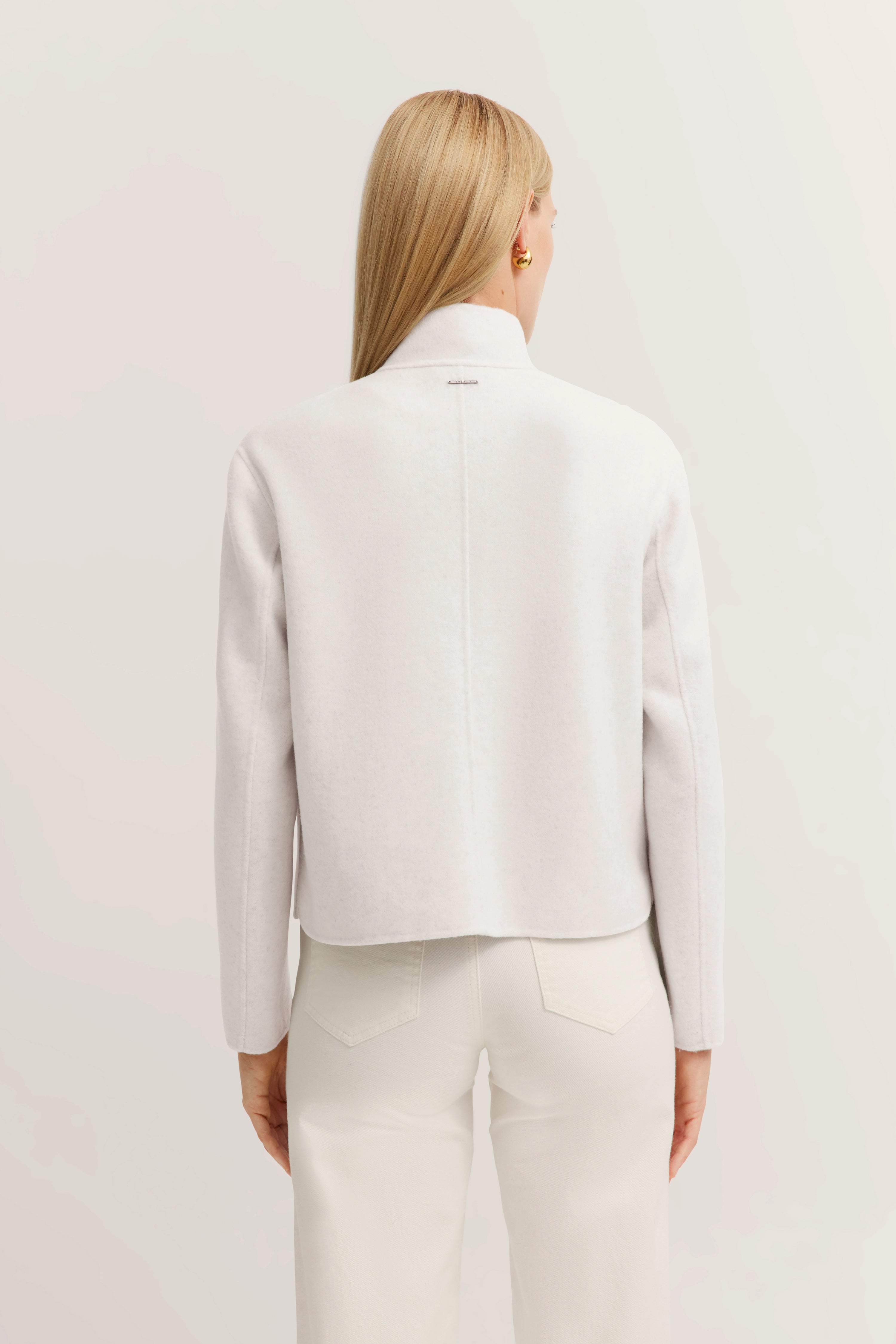 Witte bugatti jas van achteren, gedragen door model, ontspannen pose, gecombineerd met witte broek.