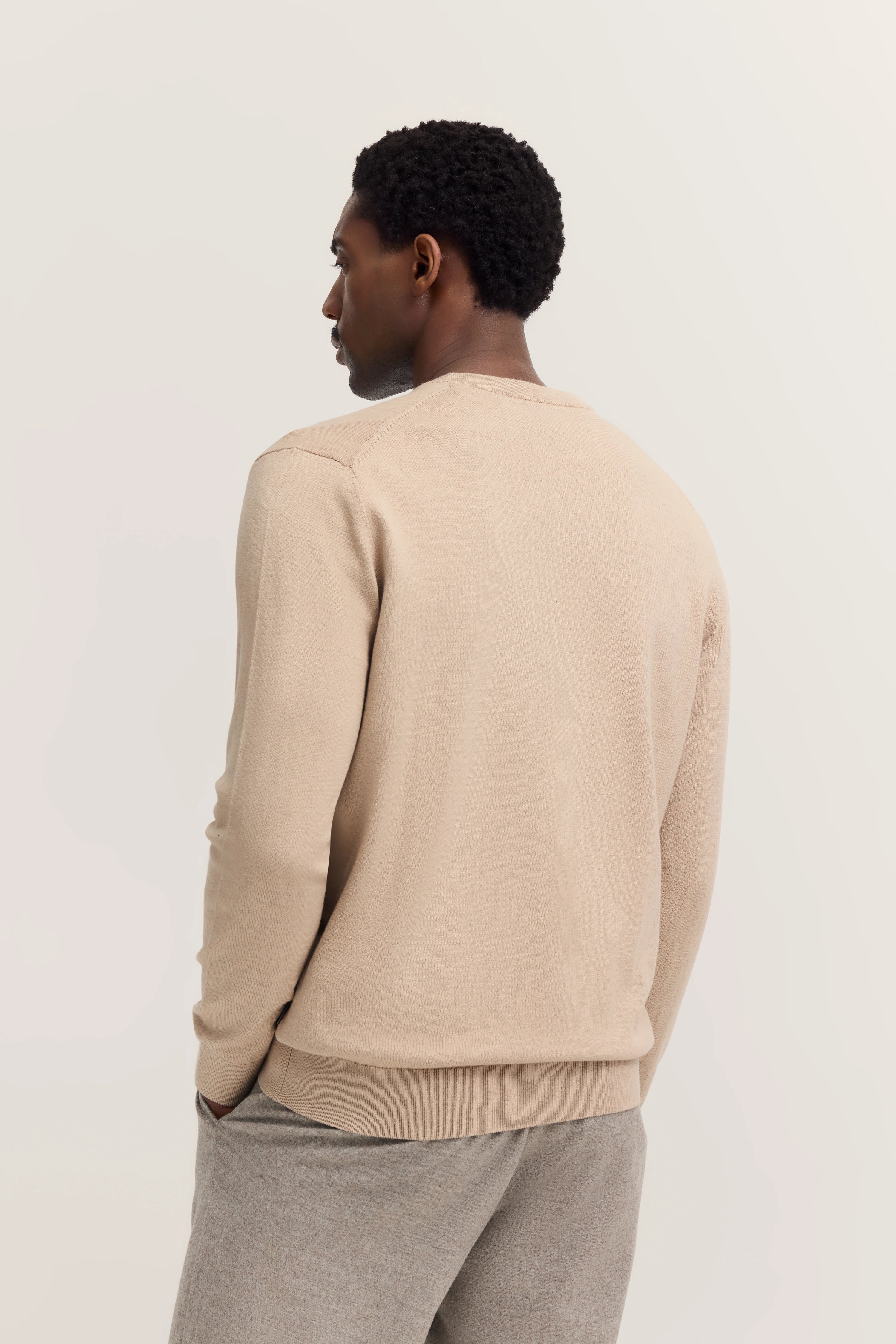 Beigefarbener Pullover und graue Hose, Modelbild im Profil, entspanntes Posing.