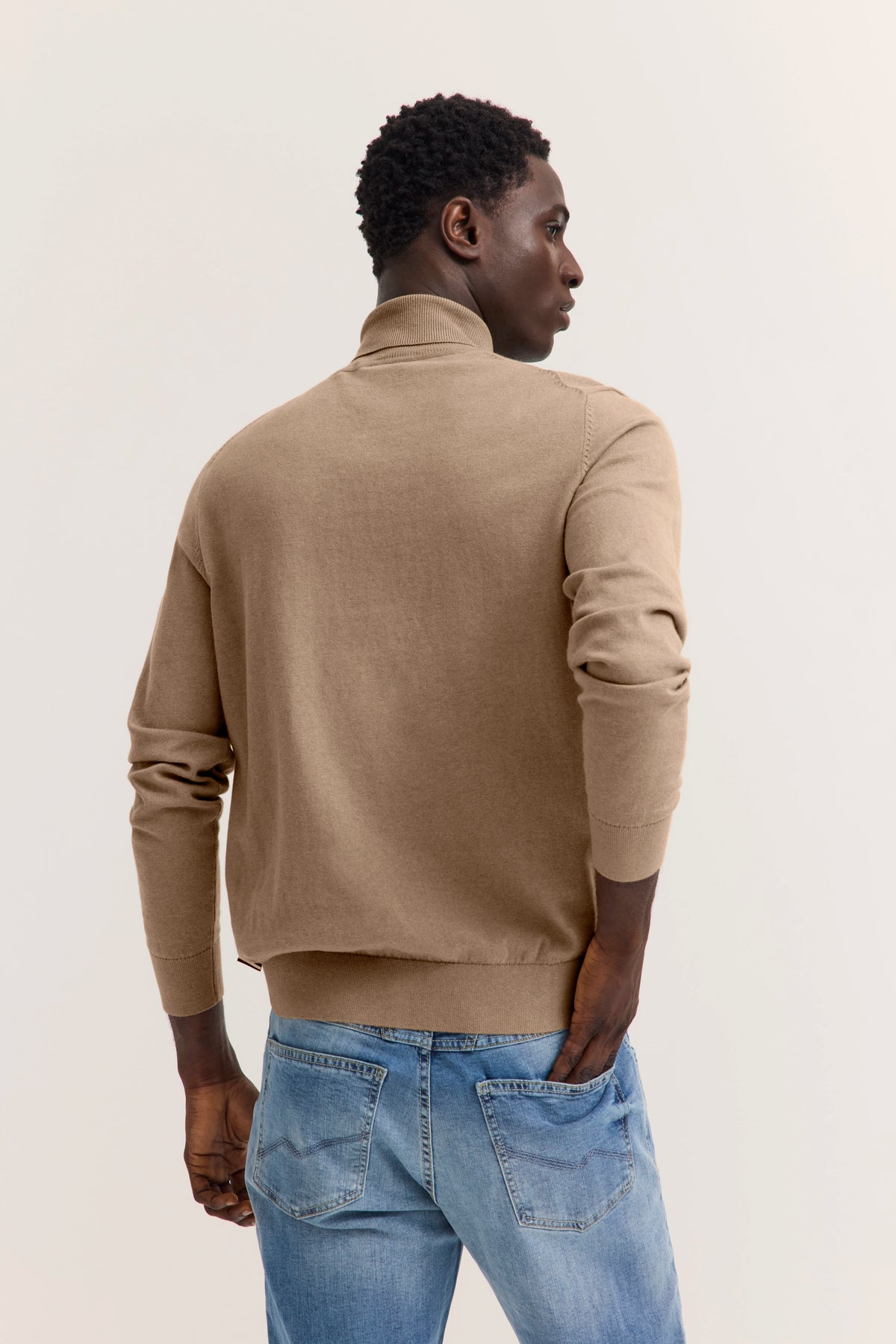 Beiges bugatti-Oberteil und blaue Jeans, Model von hinten im legeren Look.