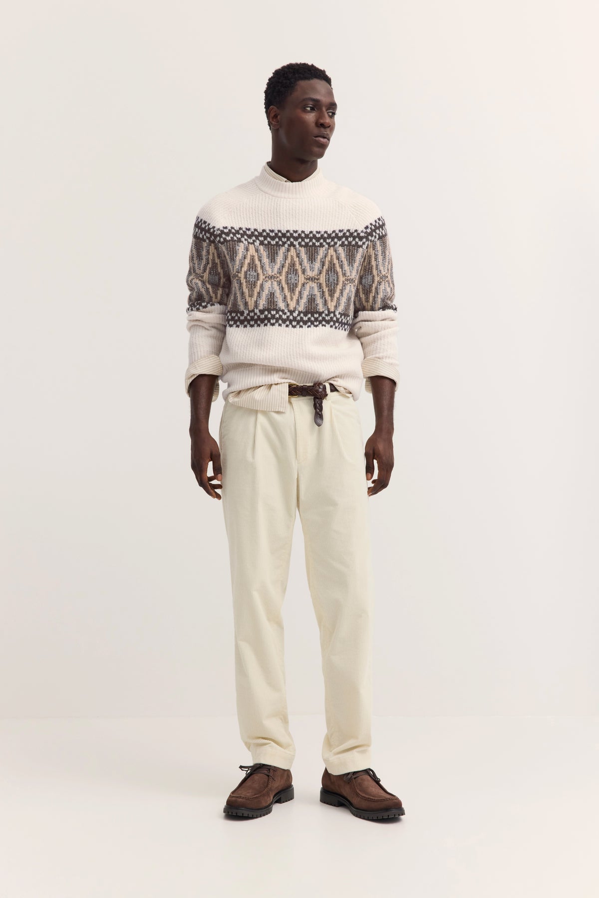 Model in cremefarbenem Pullover mit geometrischem Muster und beiger Hose, entspanntes Posing.