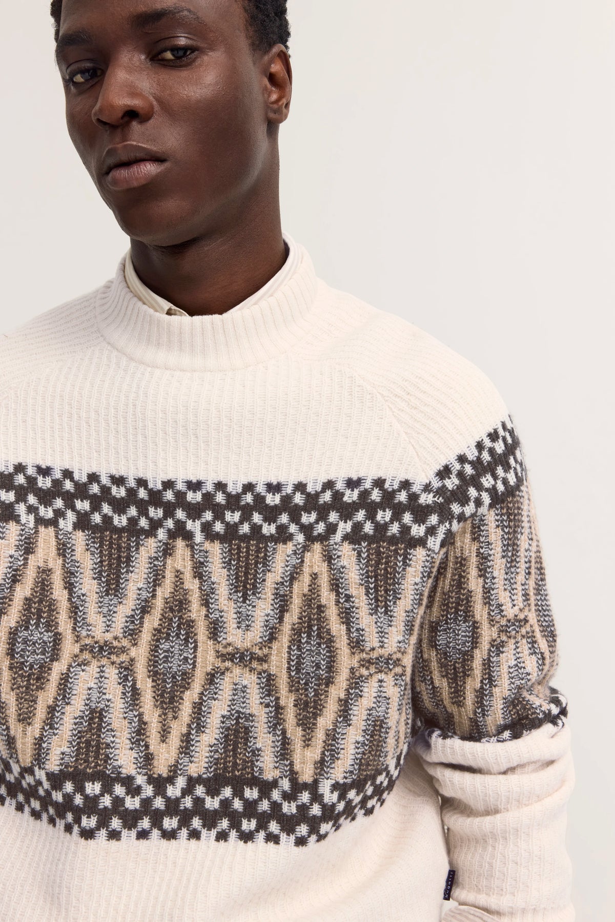 Pullover mit geometrischem Muster in Beige und Braun, Modelbild, entspannte Pose.