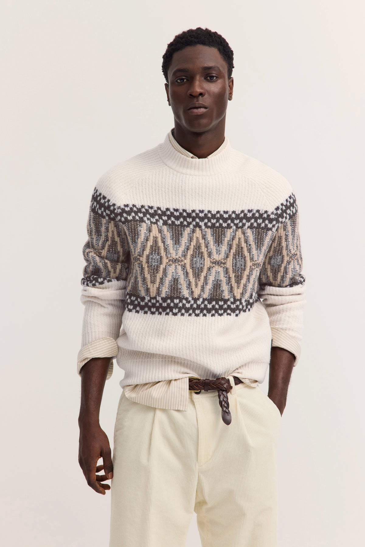 Model in cremefarbenem Pullover mit geometrischem Muster, cremefarbene Hose, legeres Posing.