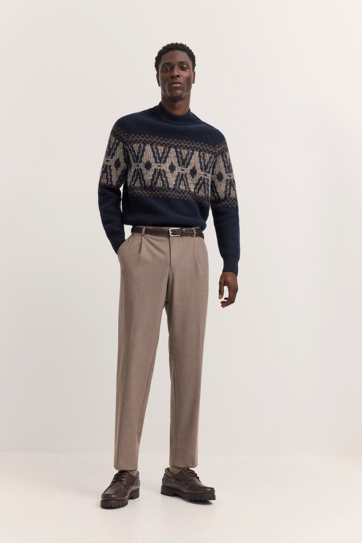 Model in beigem Anzug, blauer gemusterter Pullover, braune Schuhe. Elegantes Posing.