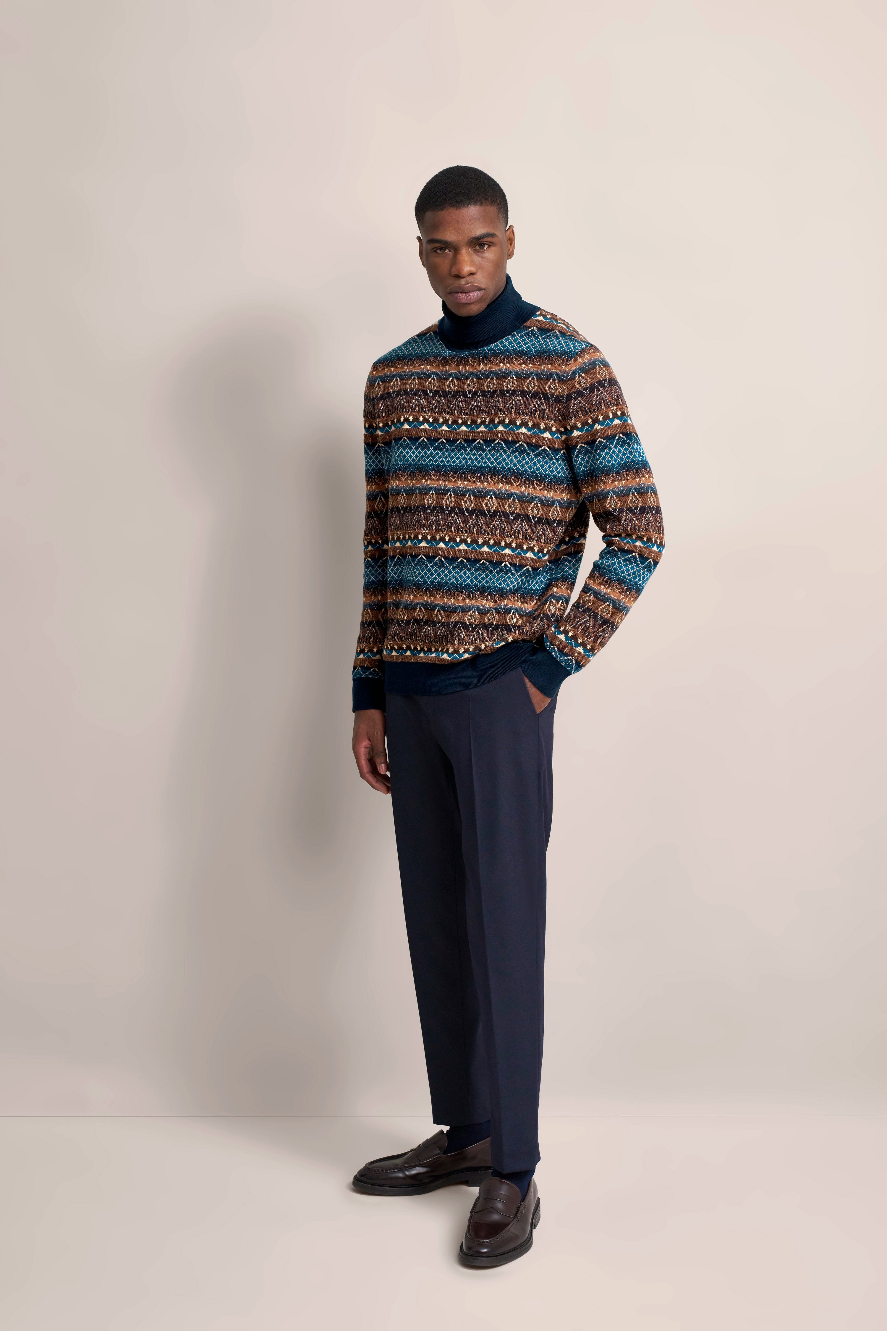Model trägt gemusterten Pullover in Blau-Braun, dunkle Hose
