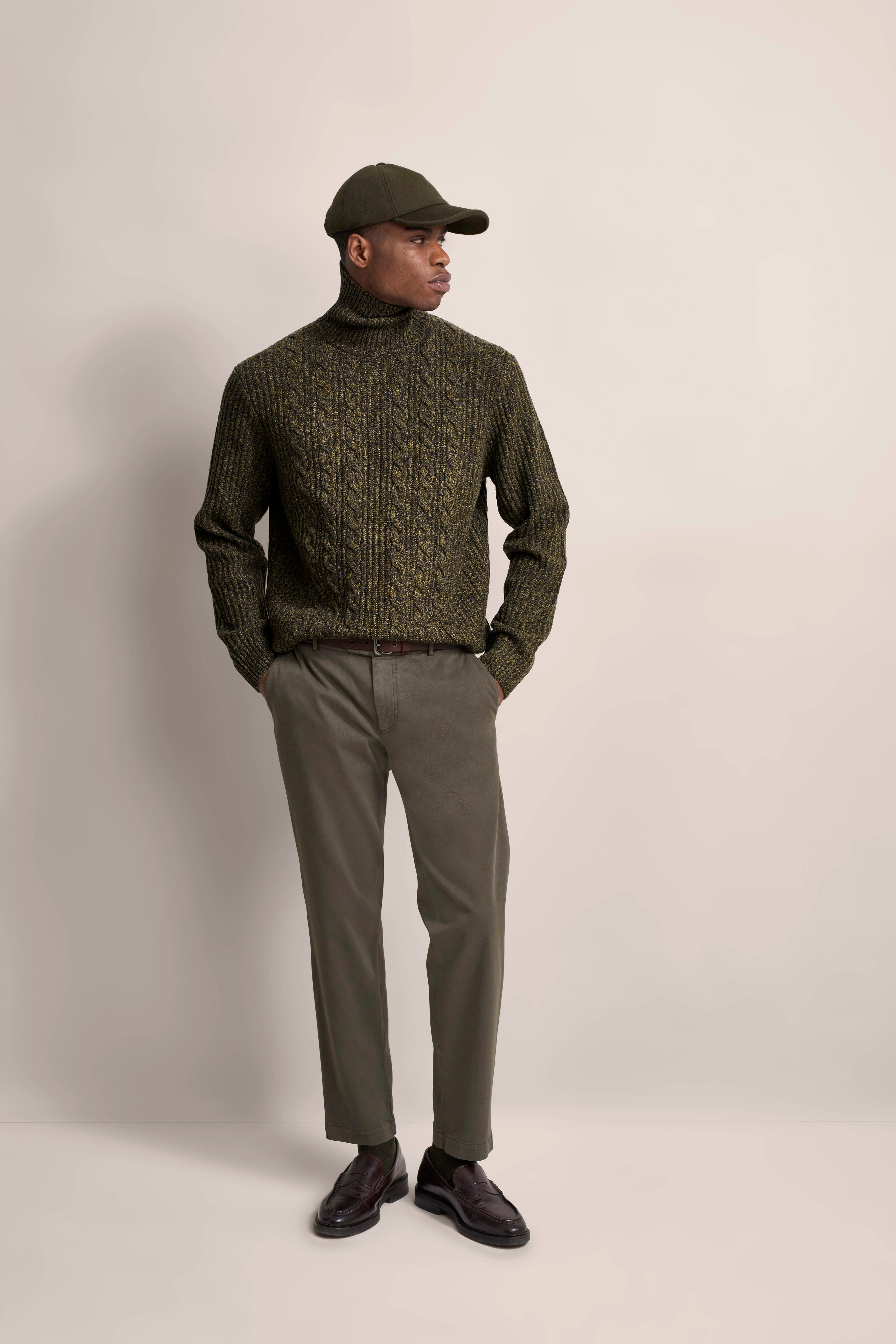 Model in olivgrünem Zopfmuster-Rollkragenpullover und Hose, seitlich posierend.