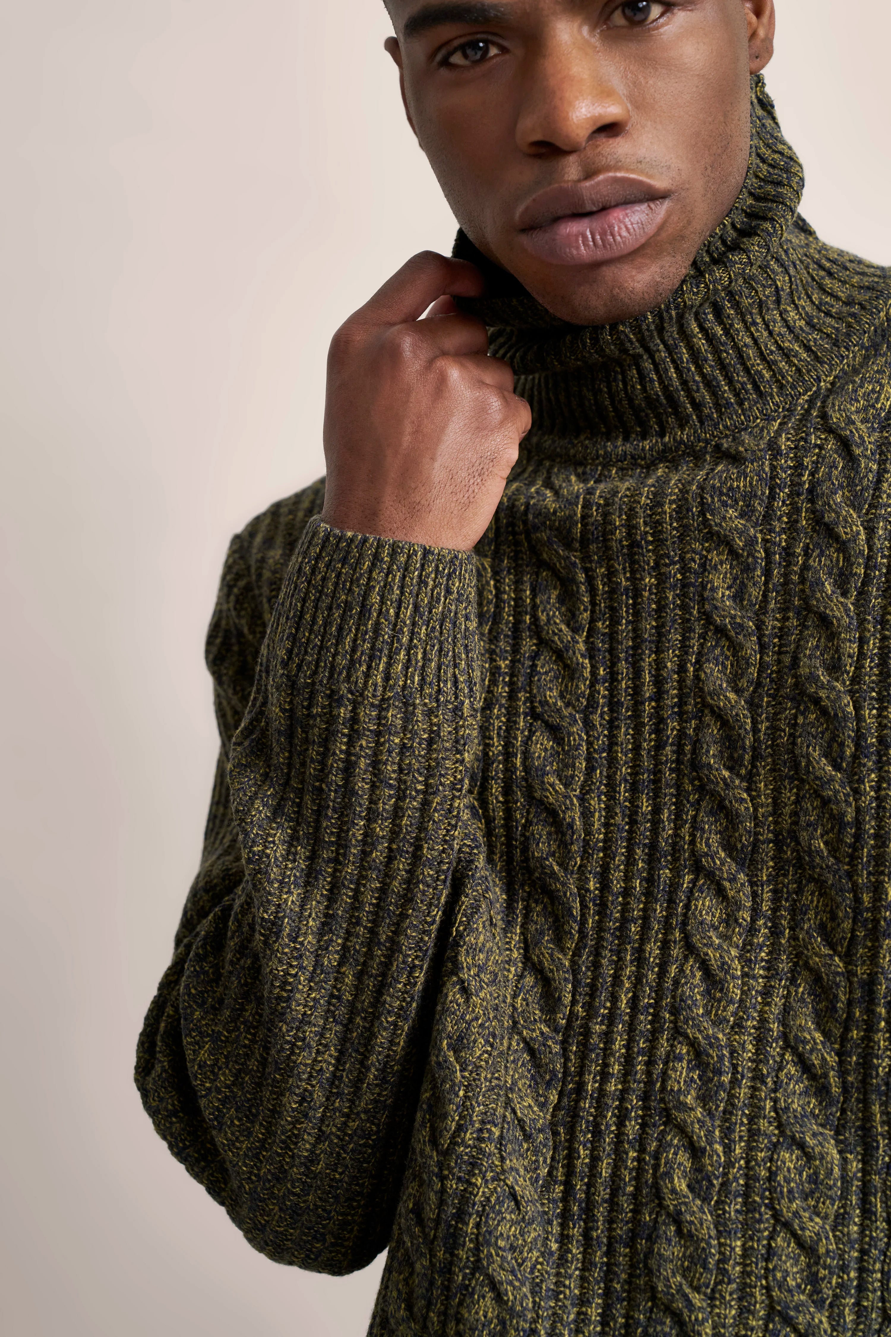 Grüner Strickpullover mit Zopfmuster, Modelbild, Hand am Rollkragen, bugatti Stil und Eleganz.