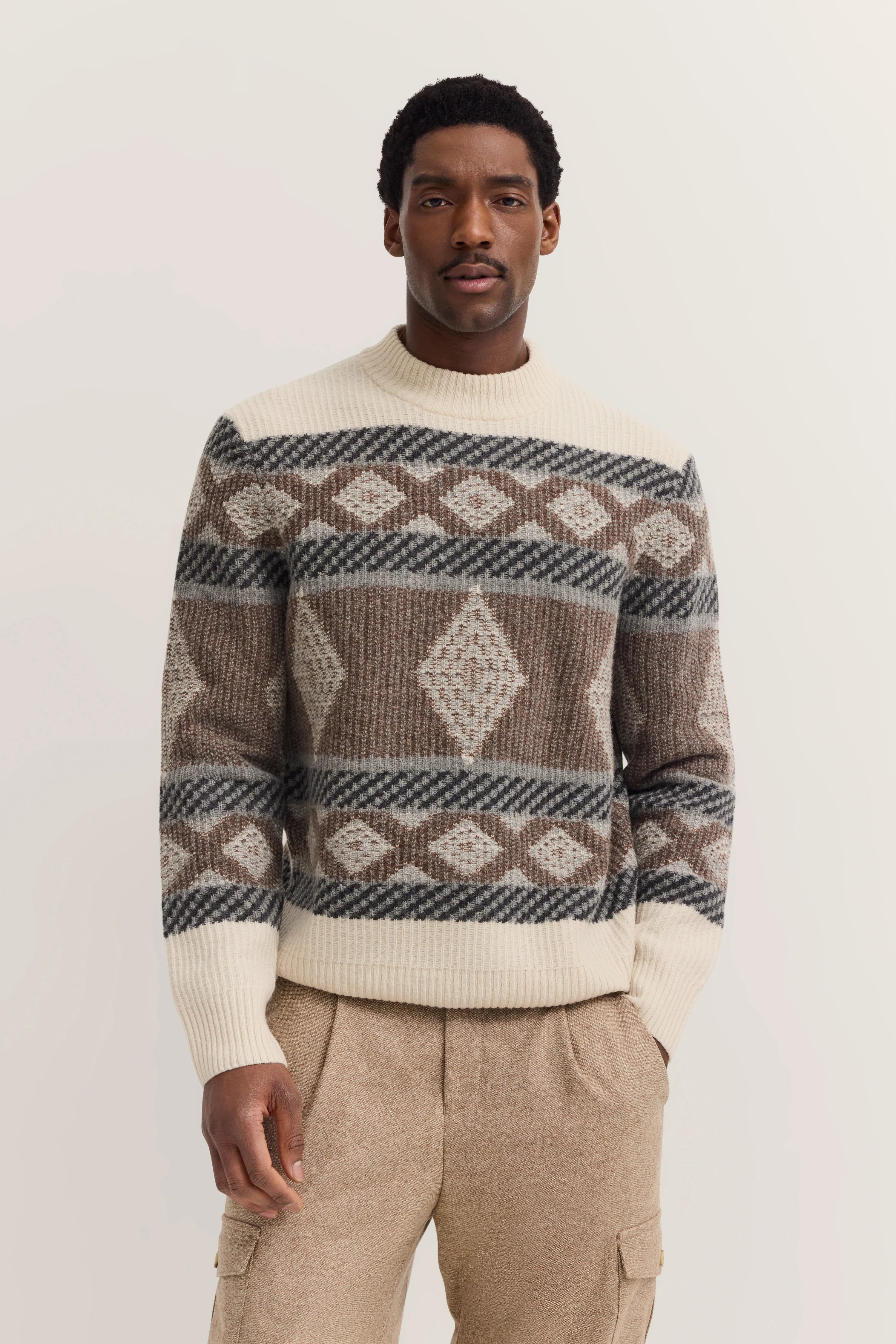 Model in gemustertem Strickpullover in Braun- und Beigetönen, legeres Posing.