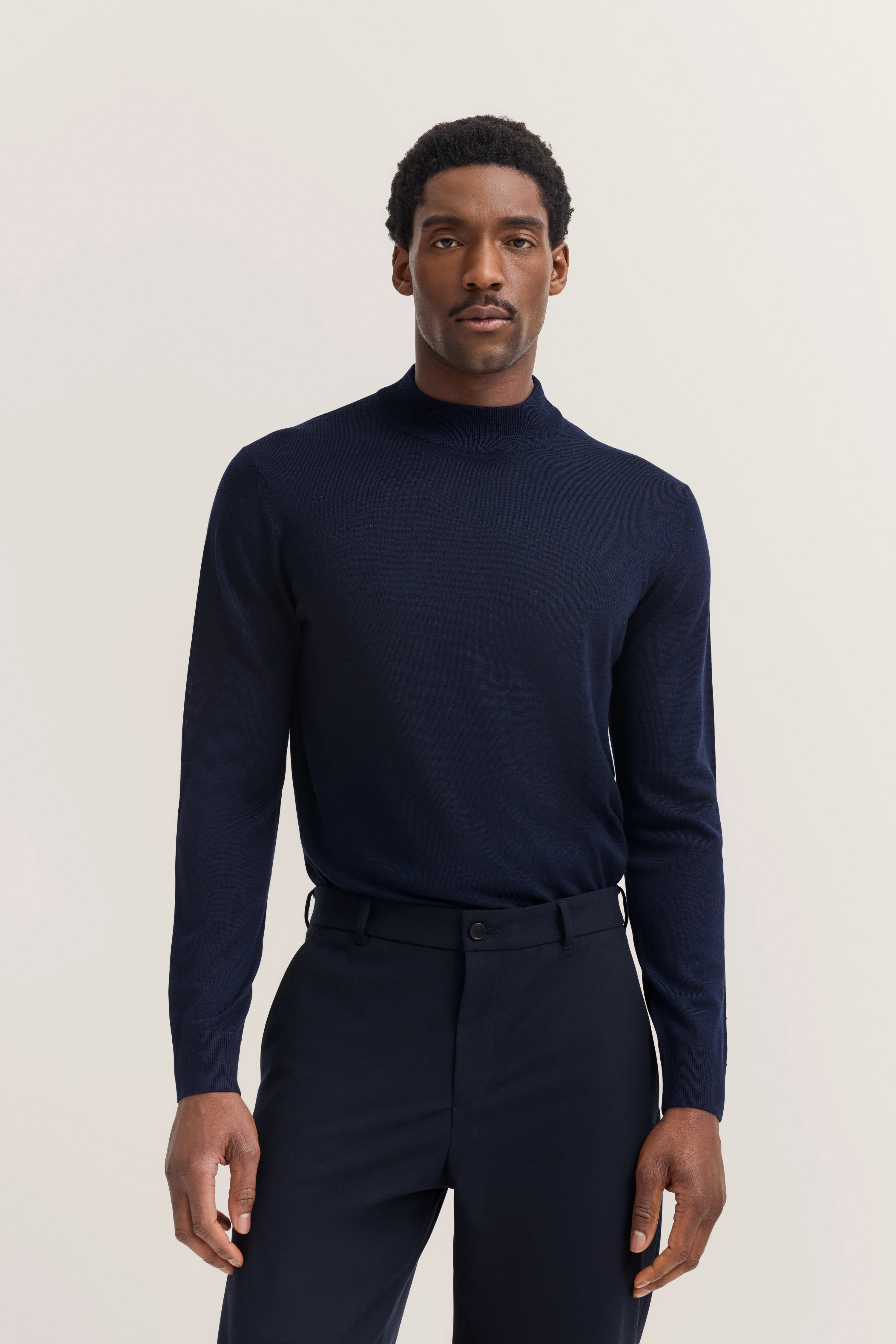 bugatti Model in dunkelblauem Rollkragenpullover und Hose, aufrecht stehend.