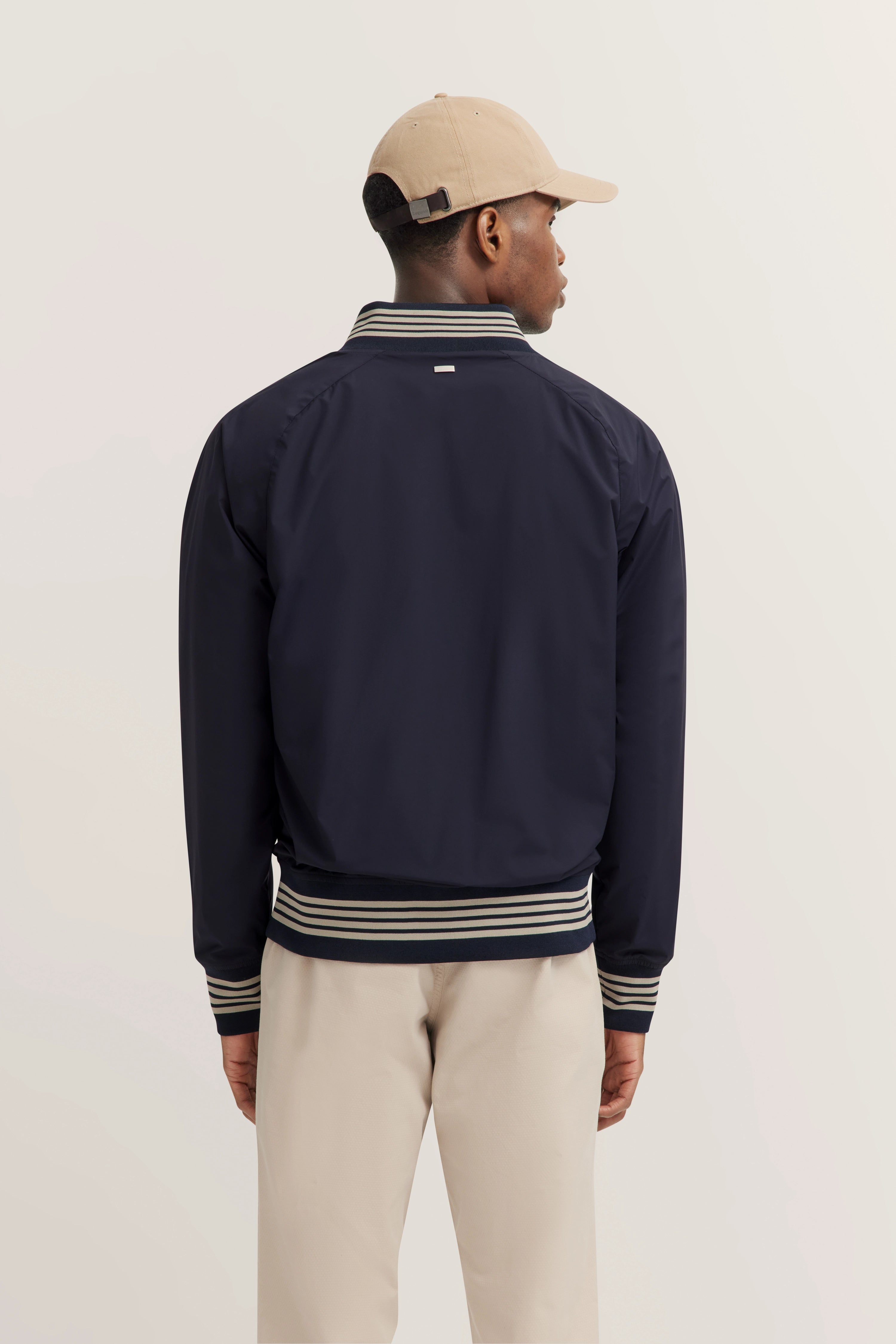 Navy Jacke mit Streifenmuster, Beige Hose und Kappe, Modelbild von hinten, entspanntes Posing.