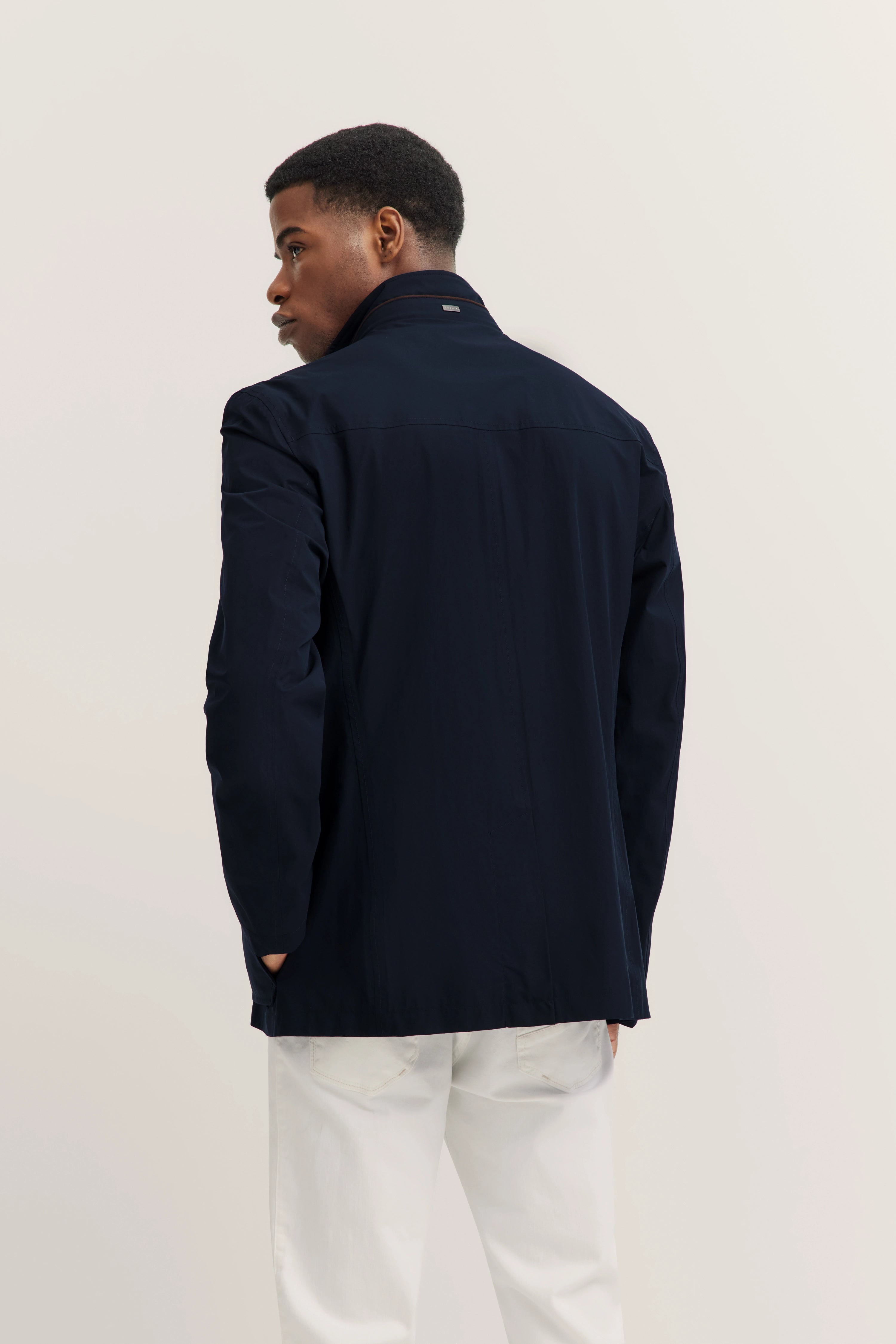 Model draagt donkerblauwe bugatti-blazer, witte broek, ontspannen pose, van achteren gefotografeerd.