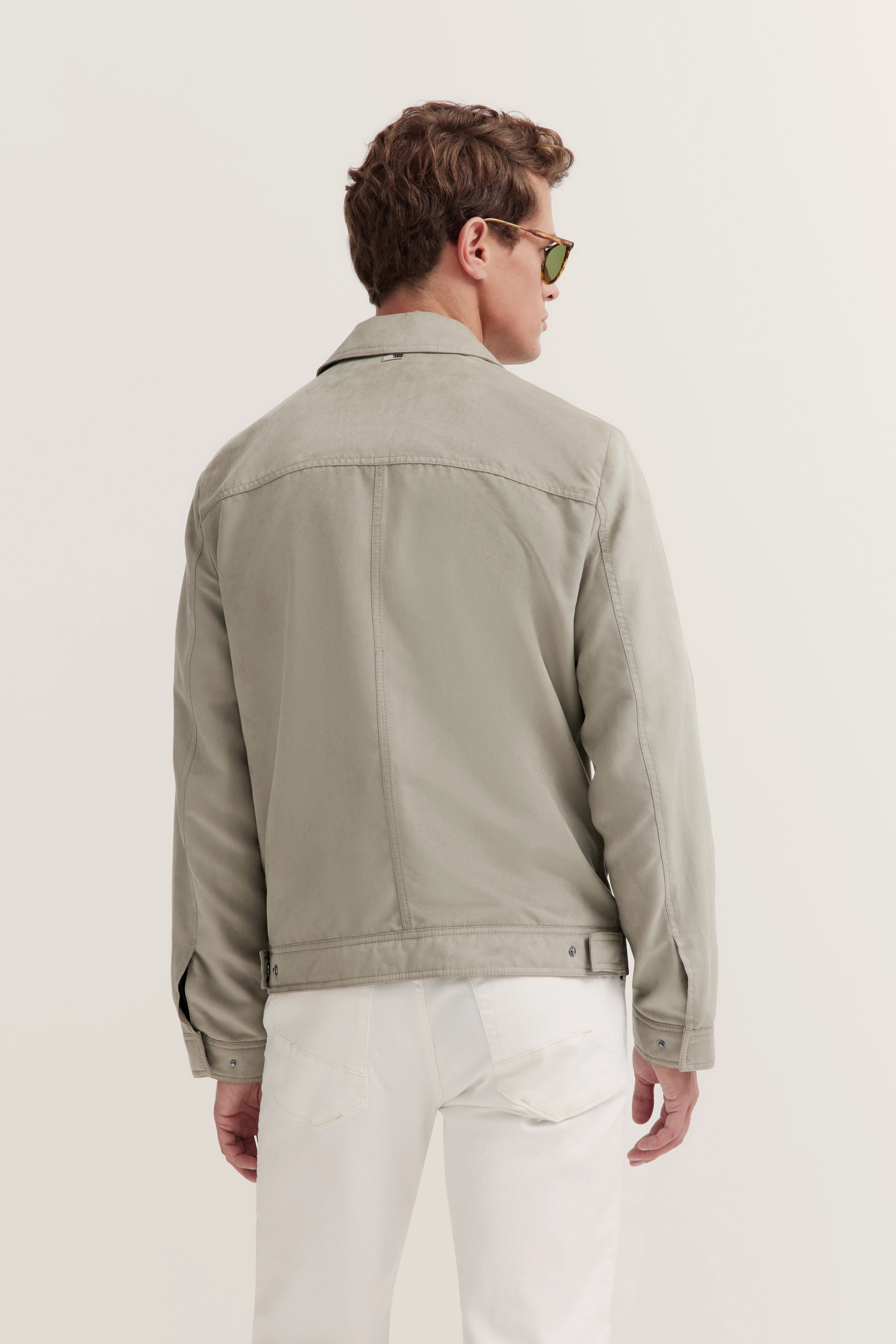 Model draagt een kaki bugatti jas en witte broek, rugaanzicht, ontspannen houding.
