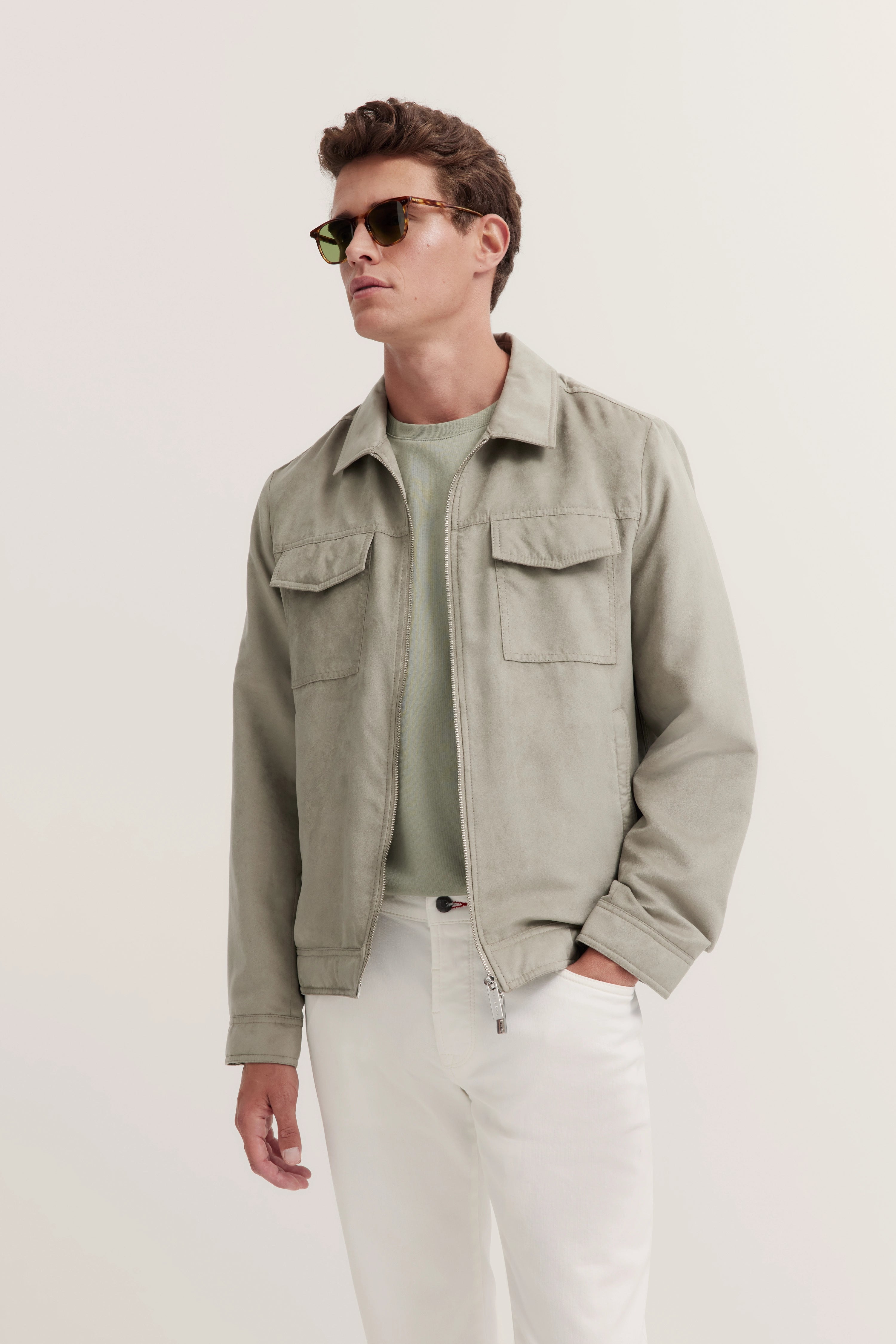 Model in lichtgroene jas, olijfgroen shirt, witte broek. Relaxte, ontspannen look van bugatti.