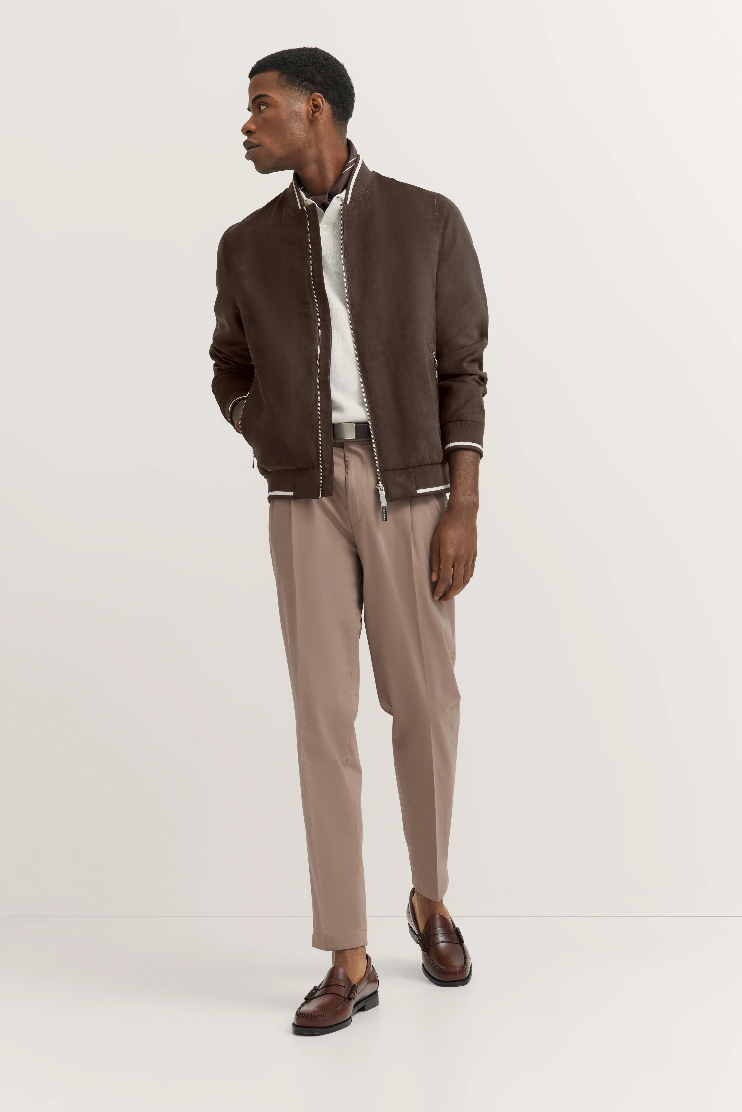 Model in brauner bugatti Jacke, weißem Shirt, beige Hose, braune Loafers, lässiges Posing.