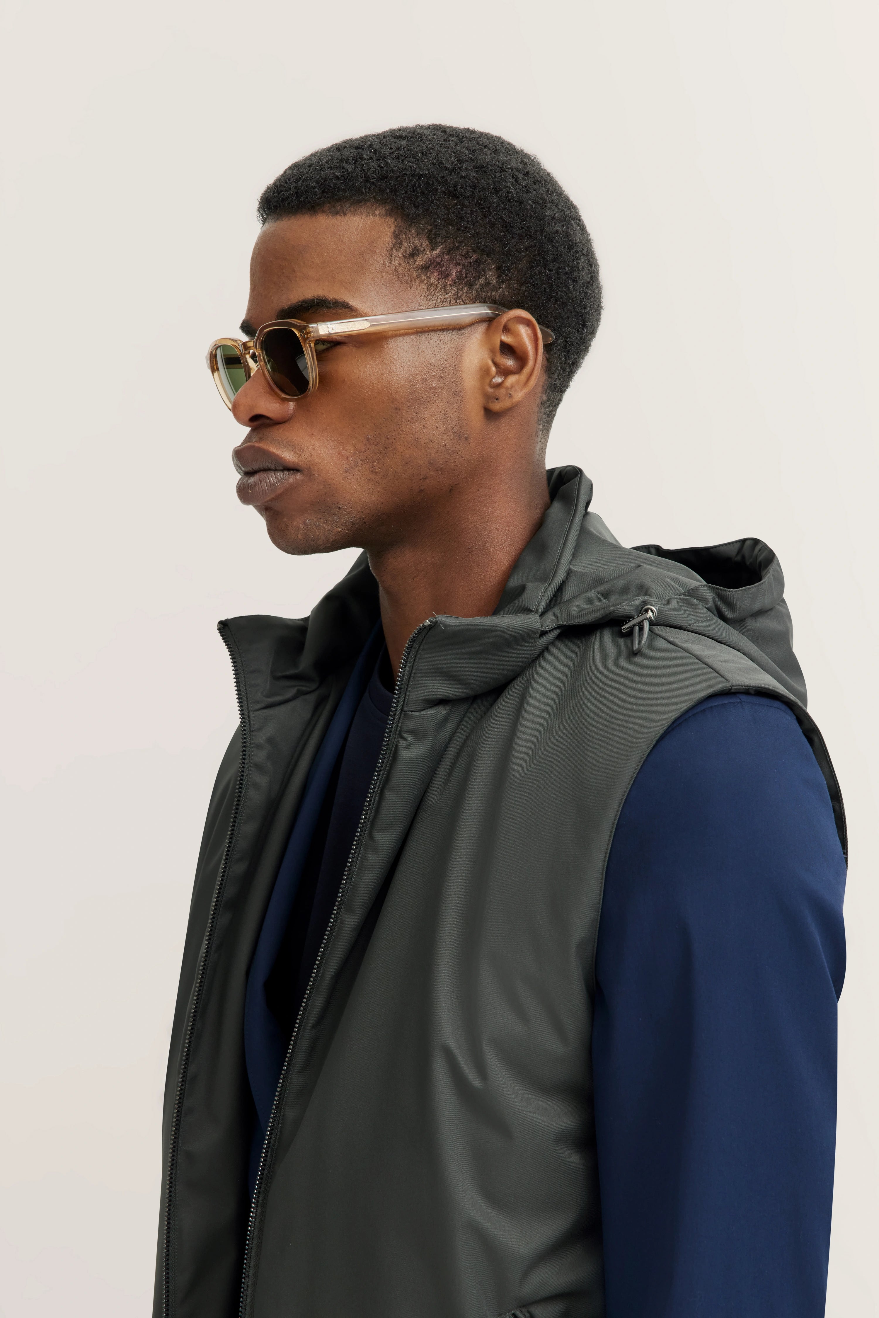 Model met donkergrijs vest en donkerblauwe top, zijwaartse pose, stijlvol en modern.