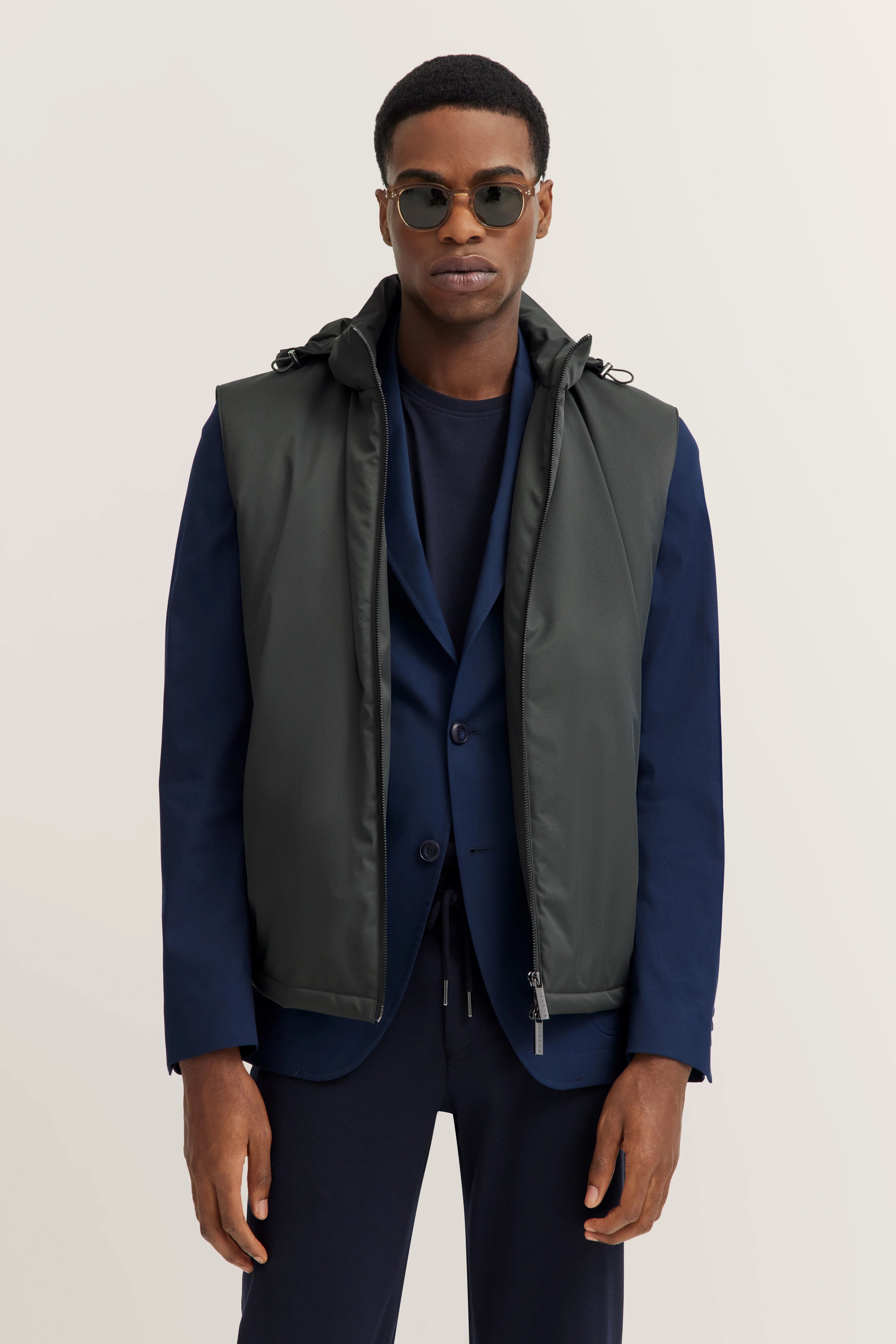Grijs vest over donkerblauw pak, casual modelpose met ontspannen houding.