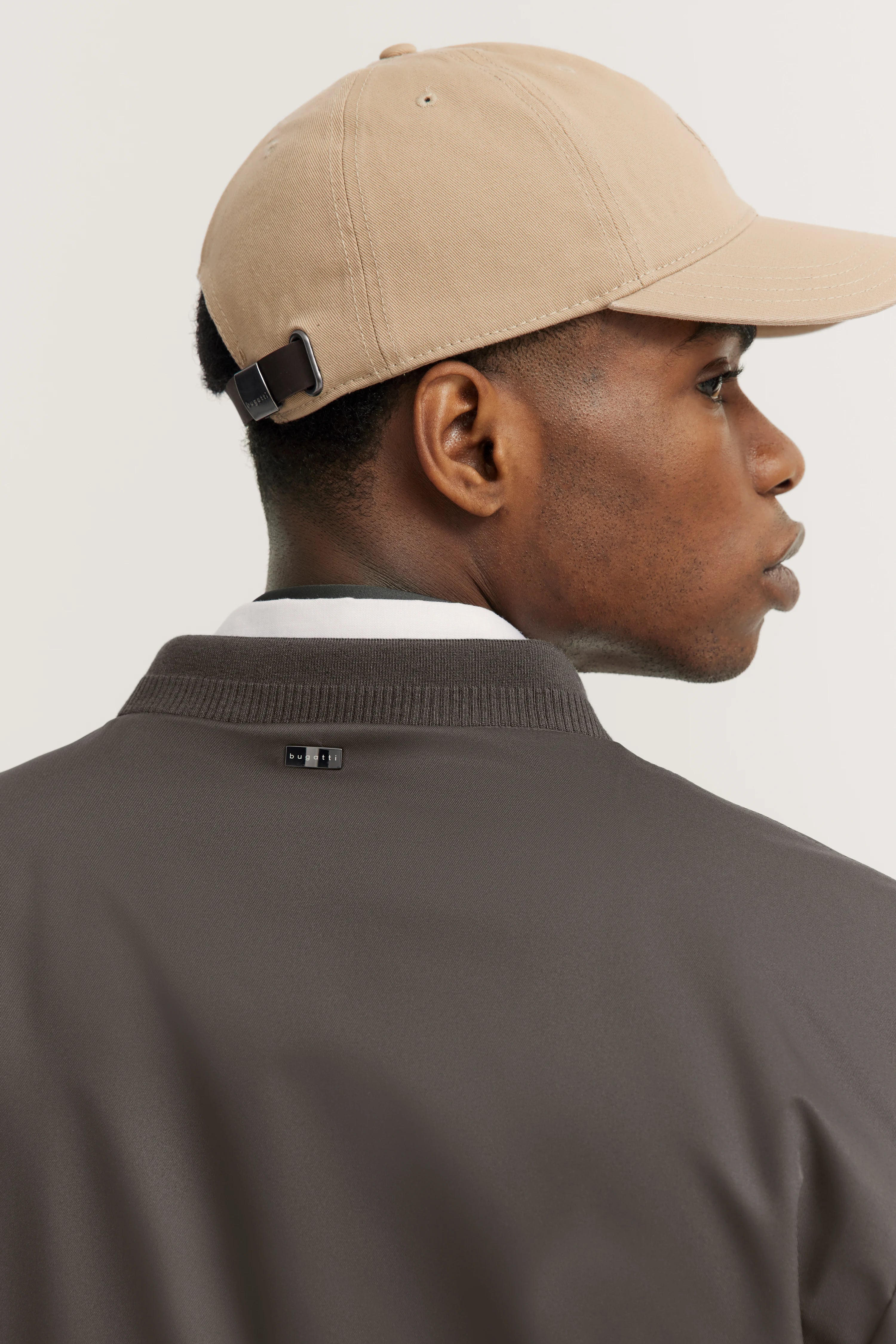Beige pet, bruine jas met bugatti-logo, model zijaanzicht, ontspannen houding.