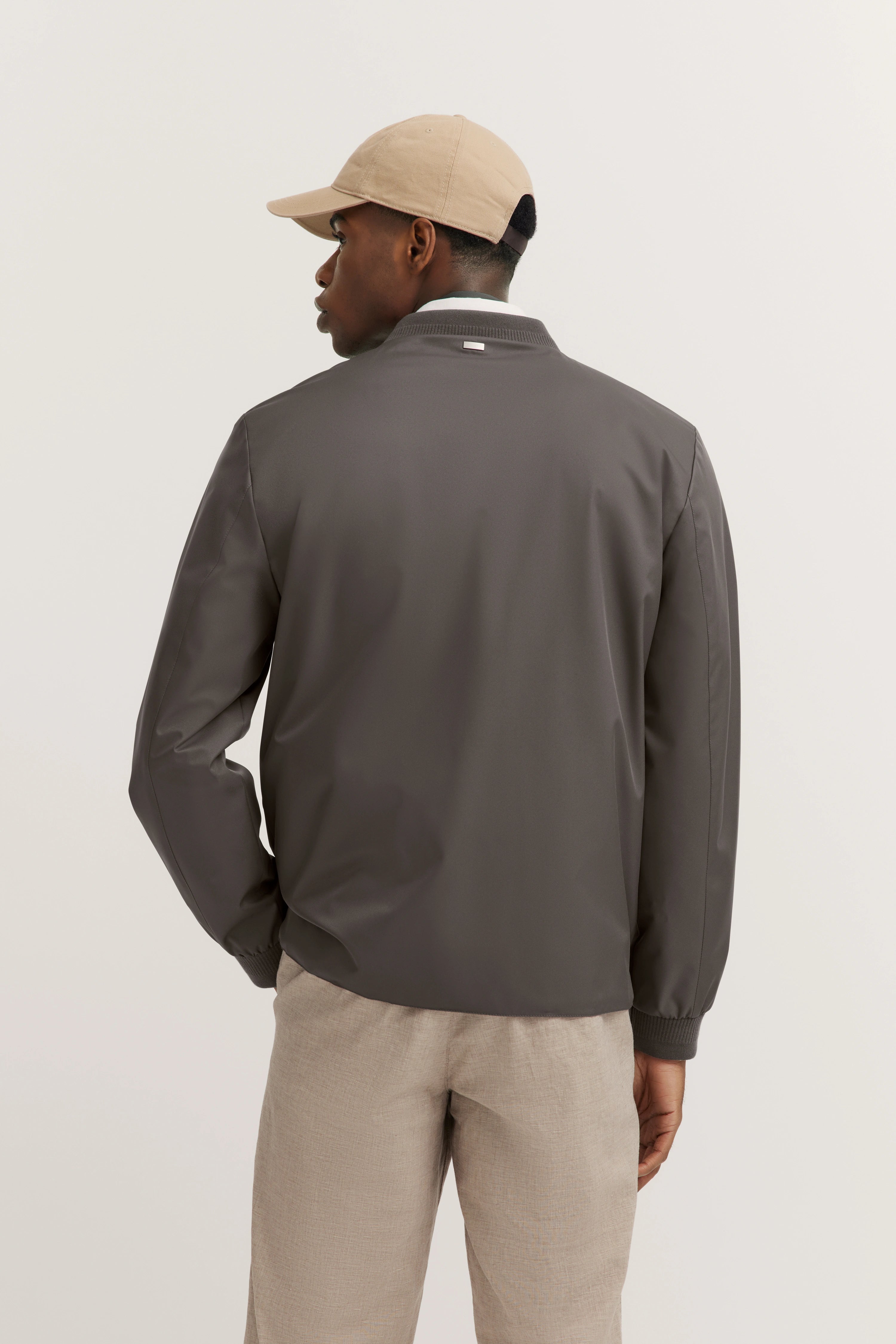 Model in casual look, grijze jas, beige broek, beige pet, achteraanzicht, bugatti stijl.