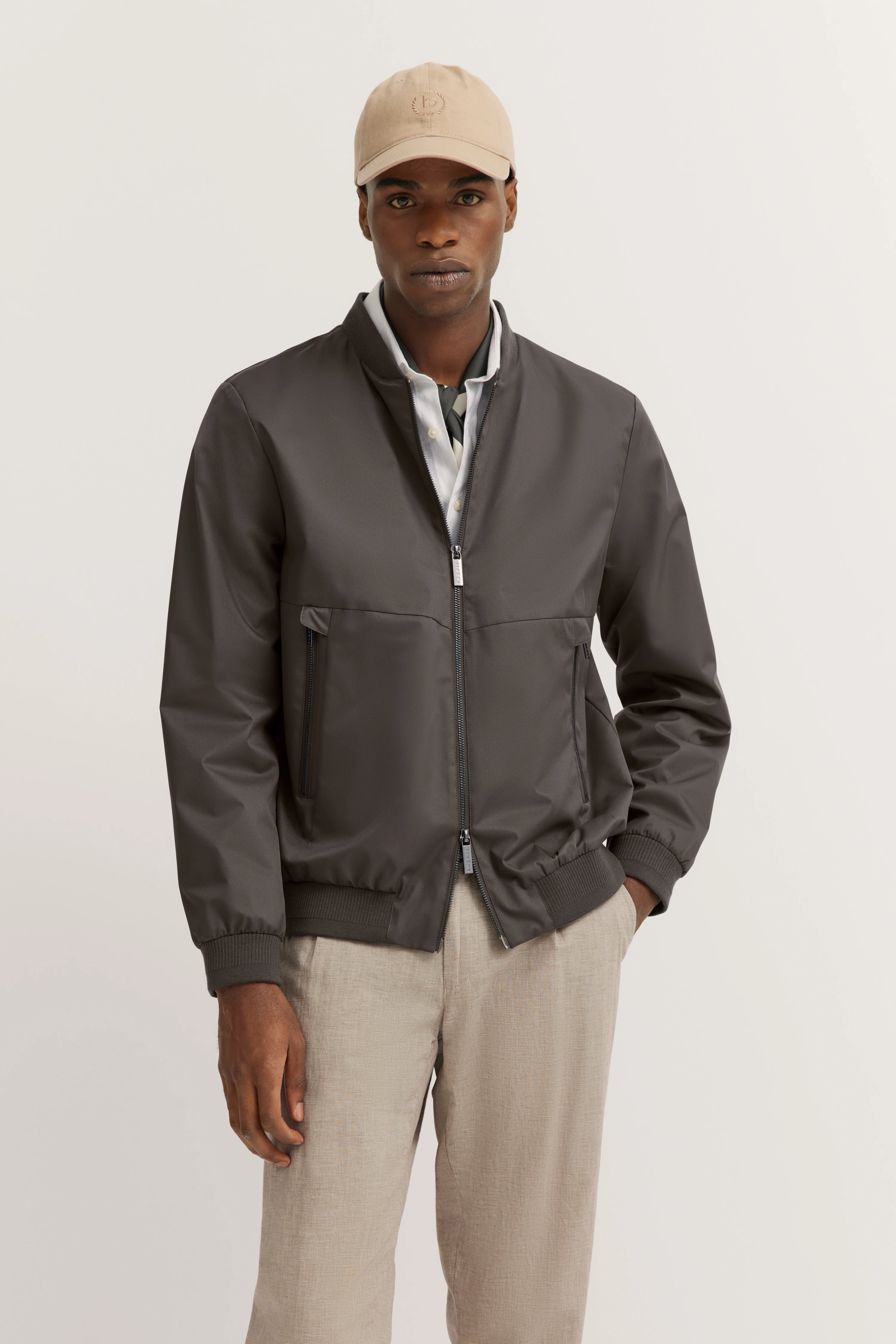 Model in grijs bugatti bomberjack, beige broek, beige pet, ontspannen pose, stedelijke stijl.