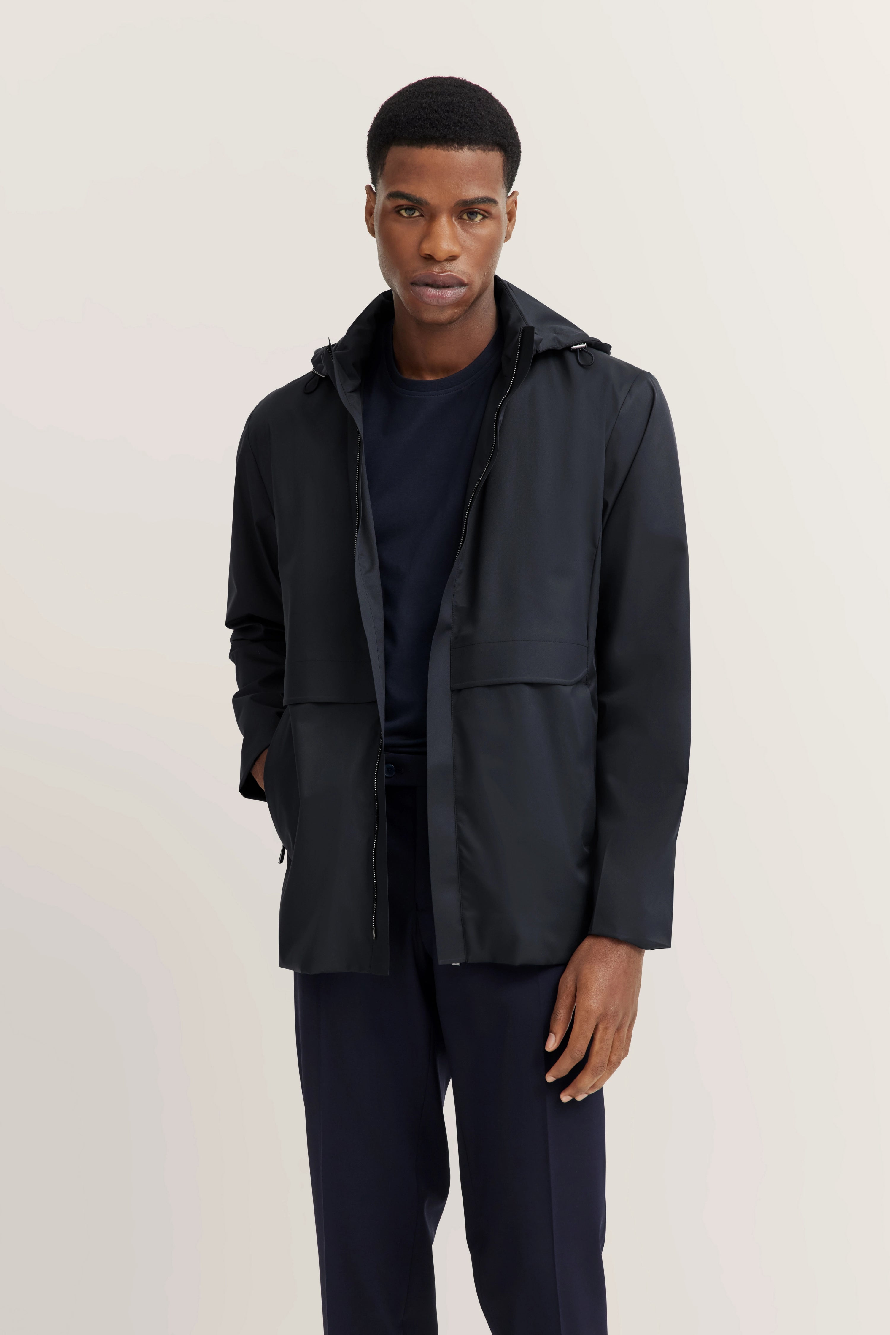 bugatti modelbeeld: man in zwarte jas en broek, ontspannen pose, stijlvol en minimalistisch.