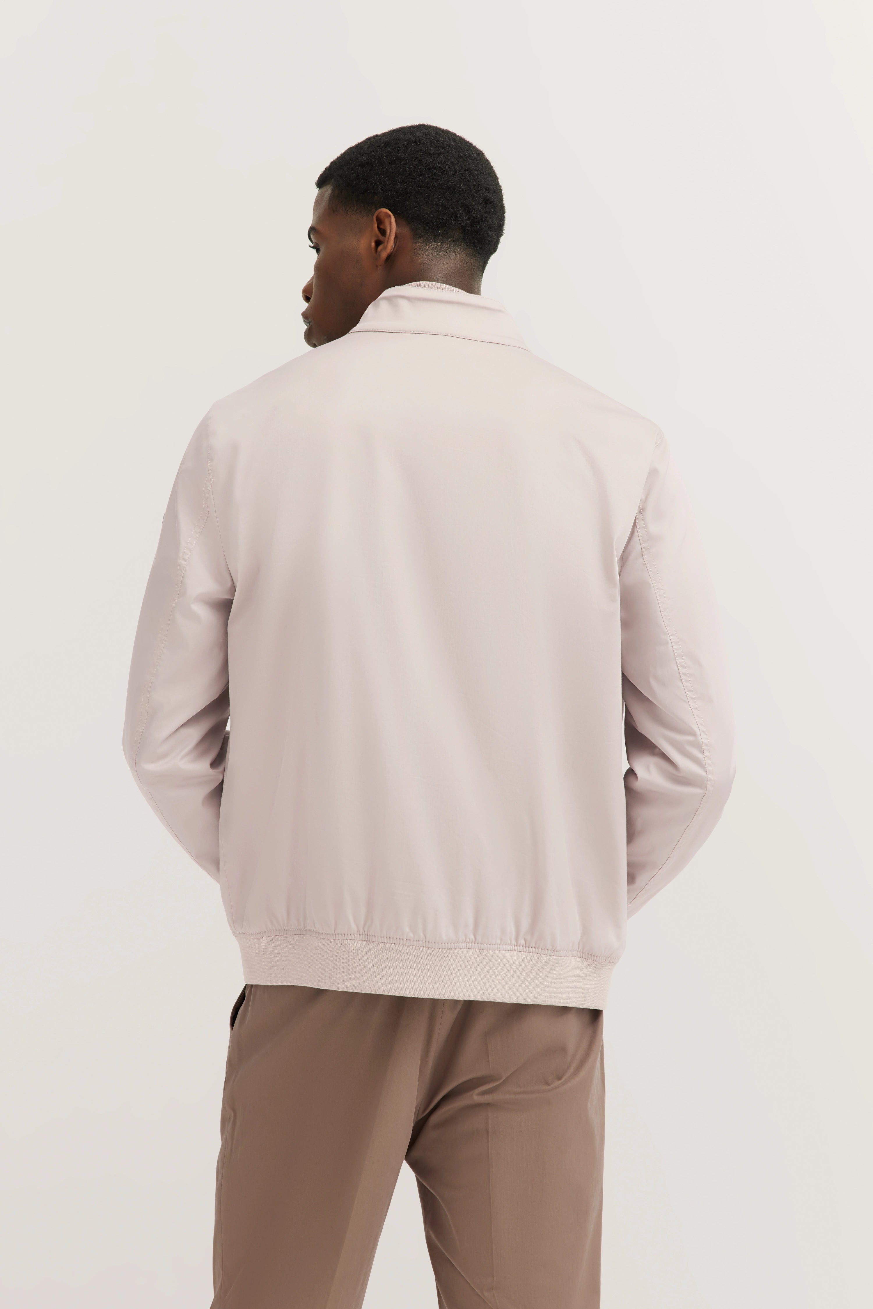 Rückansicht eines Modelbilds: hellbeige bugatti Jacke, braune Hose, entspannte Haltung.